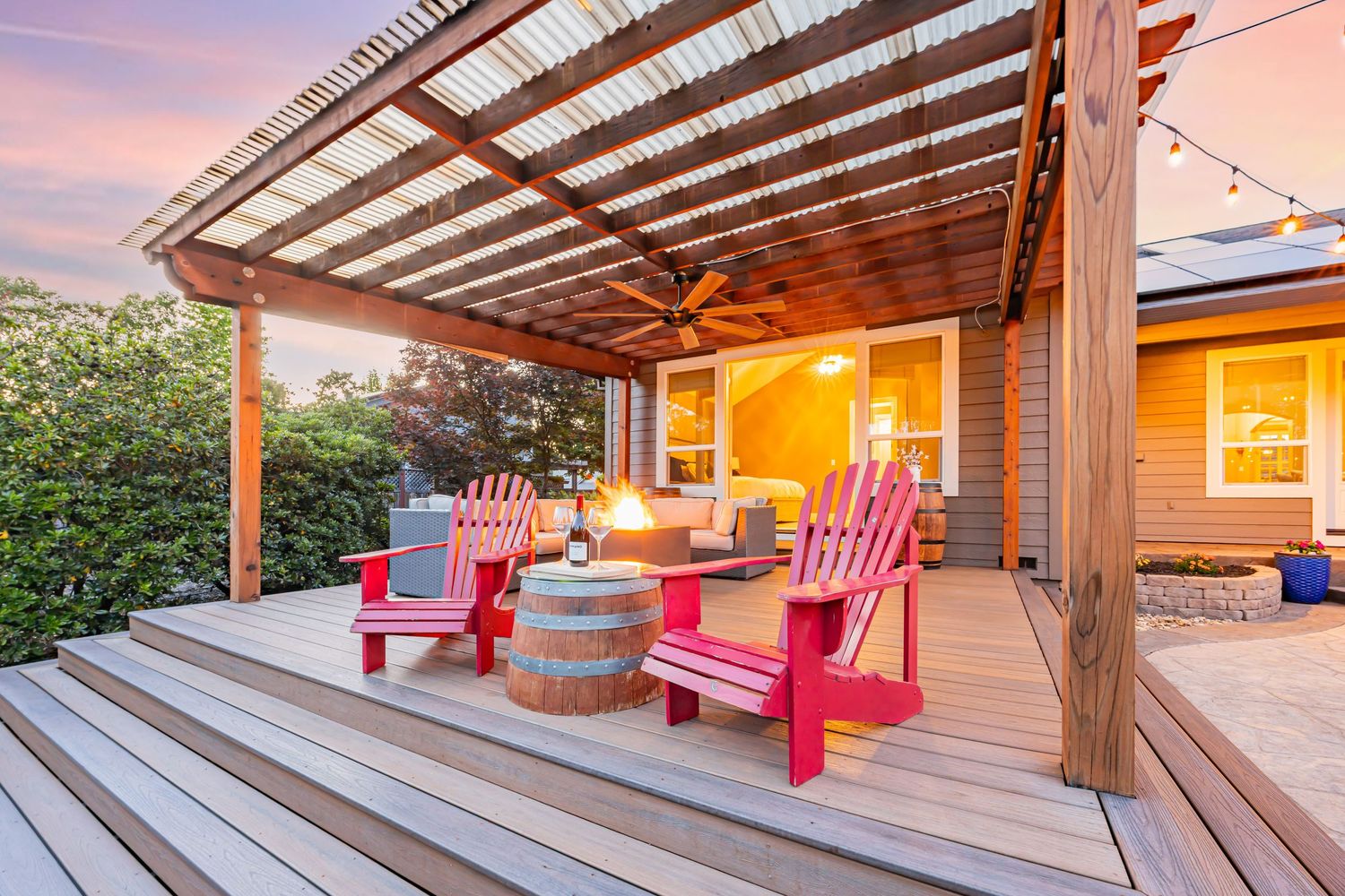 Covered deck with bright red Adirondack chairs and wine barrel table creates cozy outdoor seating area.