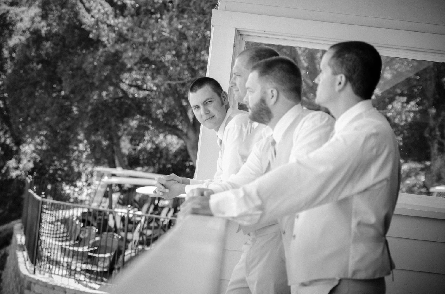 Three groomsmen in white suits enjoying refreshments on a porch.