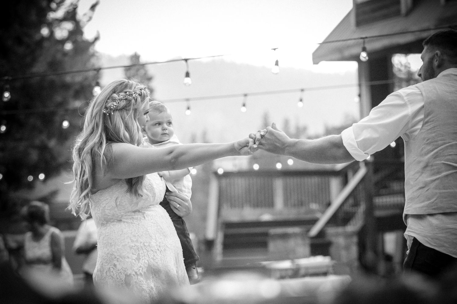 Black and white photo of a couple dancing energetically at an outdoor wedding celebration.