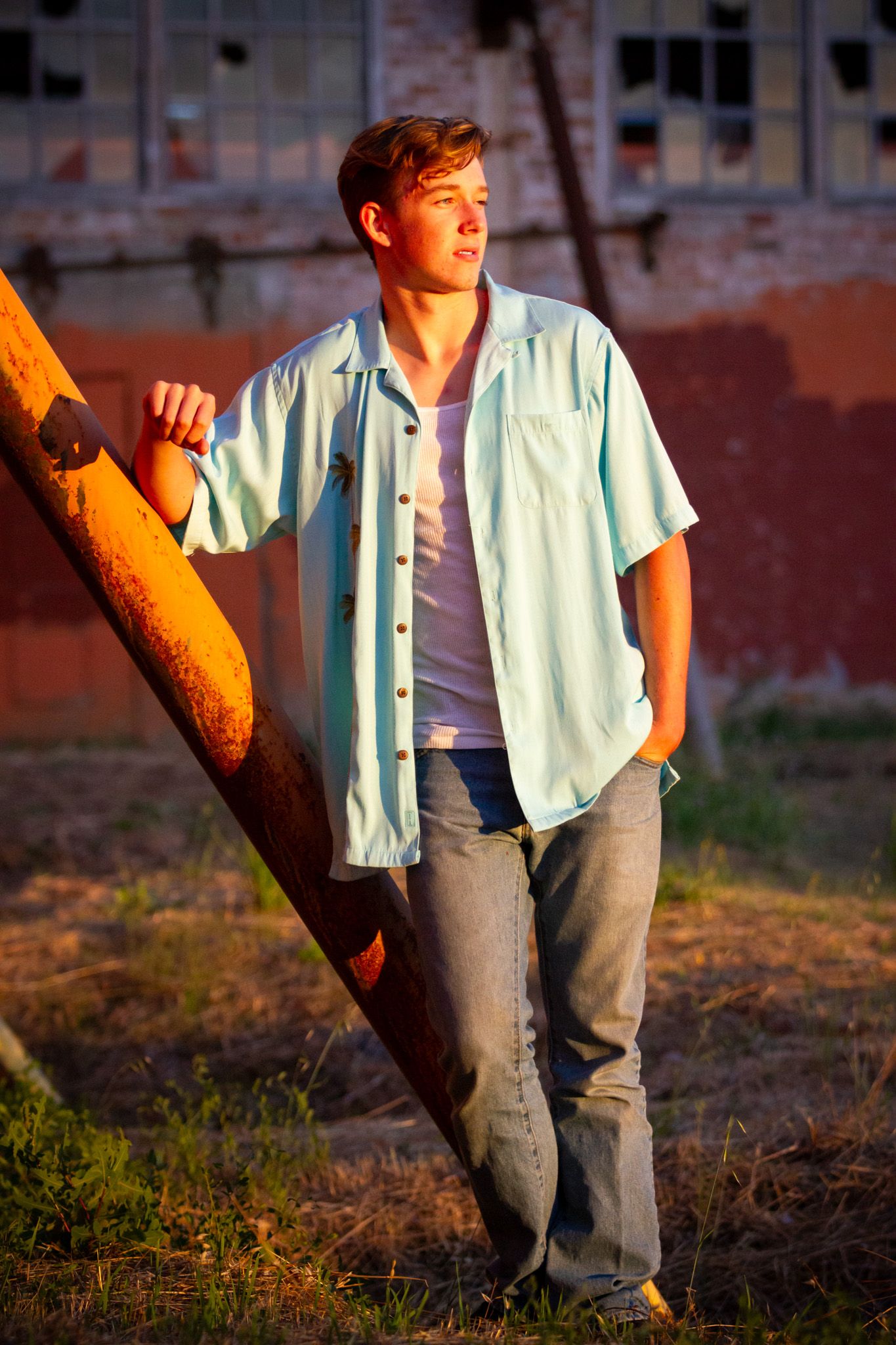 Person in light blue shirt leans against pole at sunset in urban setting.