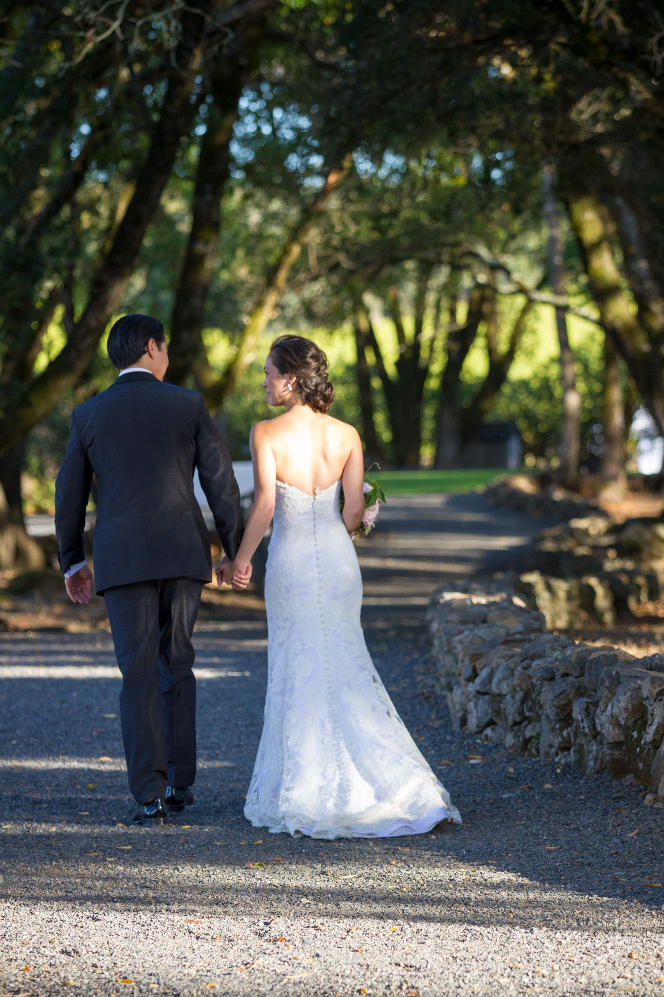 Newlywed couple walking down a tree-lined path in wedding attire.