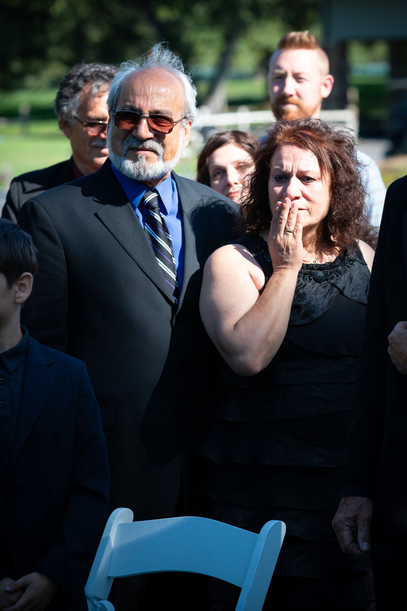 Wedding guests in formal attire show emotion during outdoor ceremony.