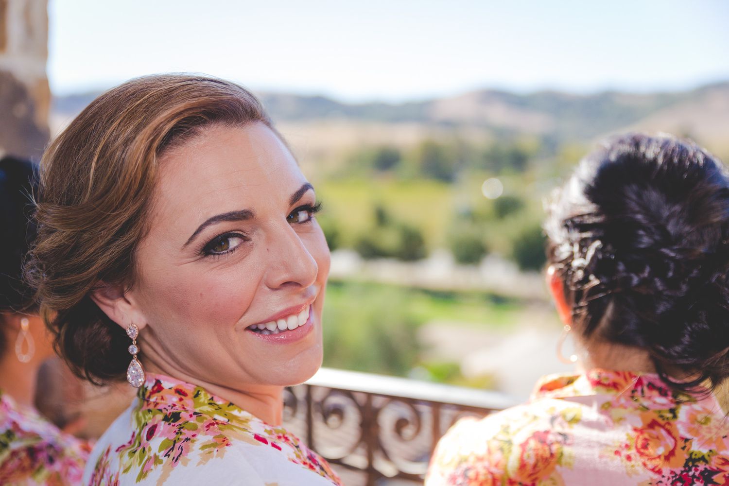 Bridal party member in floral robe smiles over shoulder against scenic mountain backdrop.
