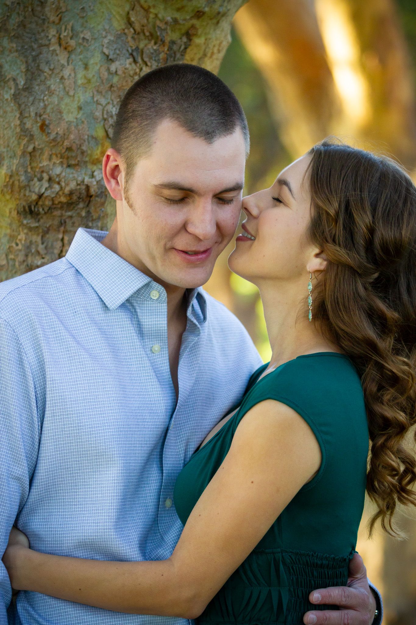 Intimate moment between couple near tree during engagement photo session.
