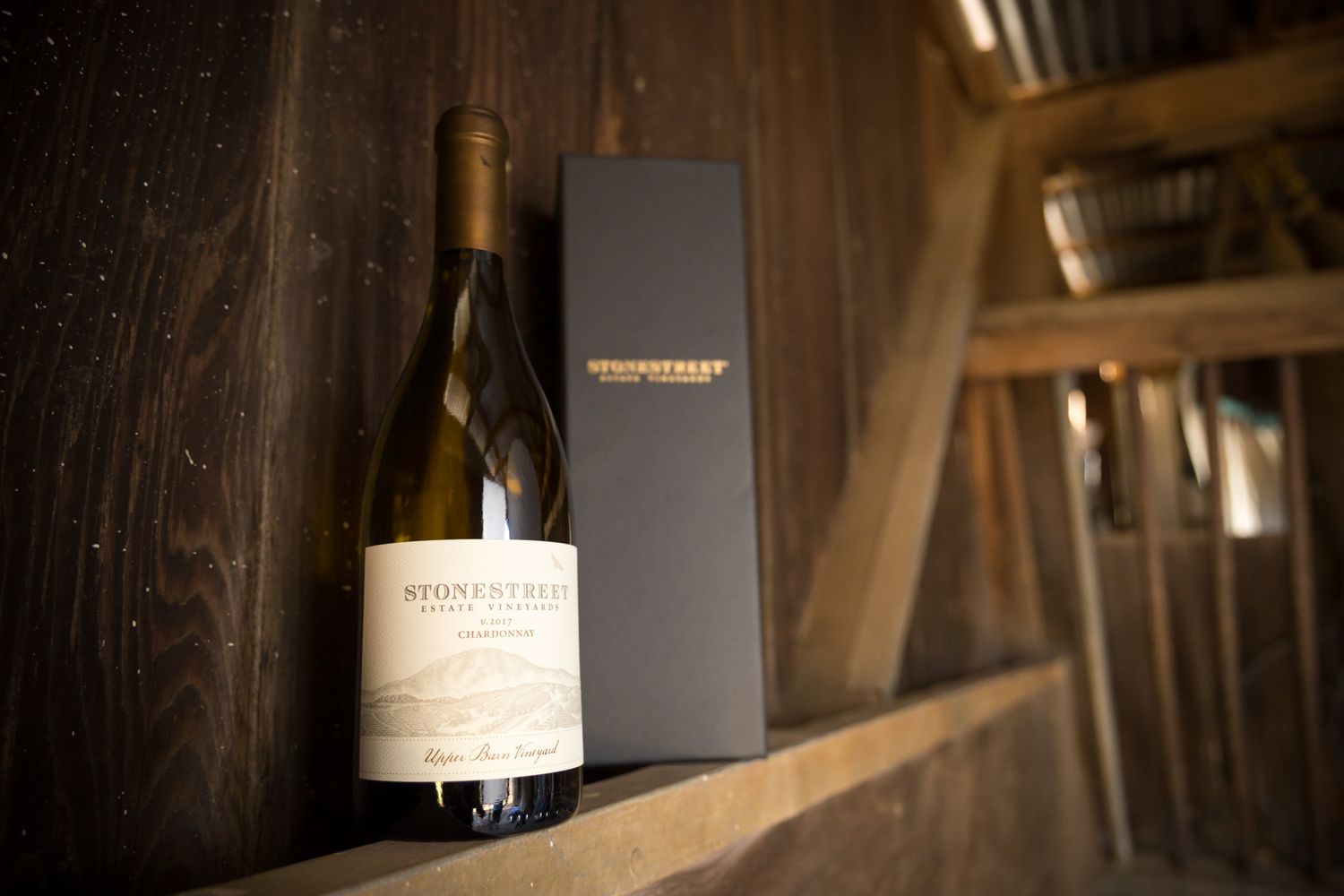 Wine bottle and black gift box arrangement on rustic wooden shelf in winery.