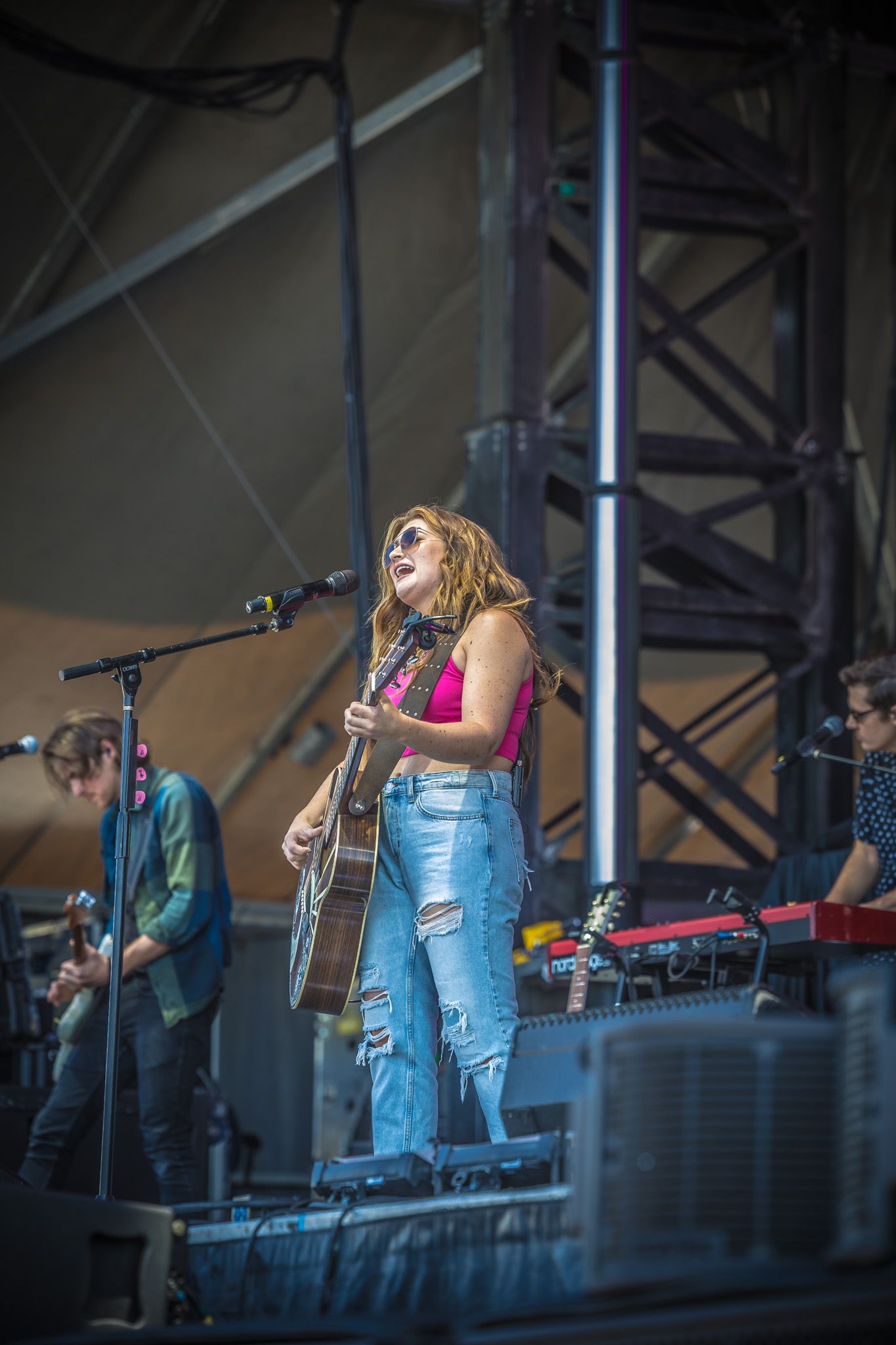 A stage performance featuring a musician in ripped jeans playing acoustic guitar under concert lighting.