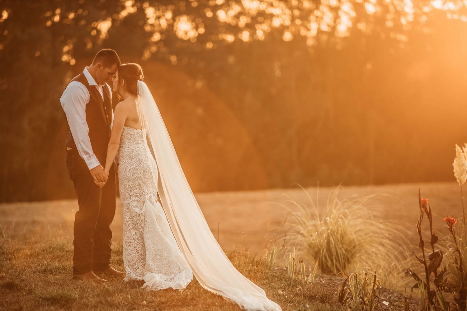 A romantic sunset silhouette of newlyweds with flowing veil against golden light.