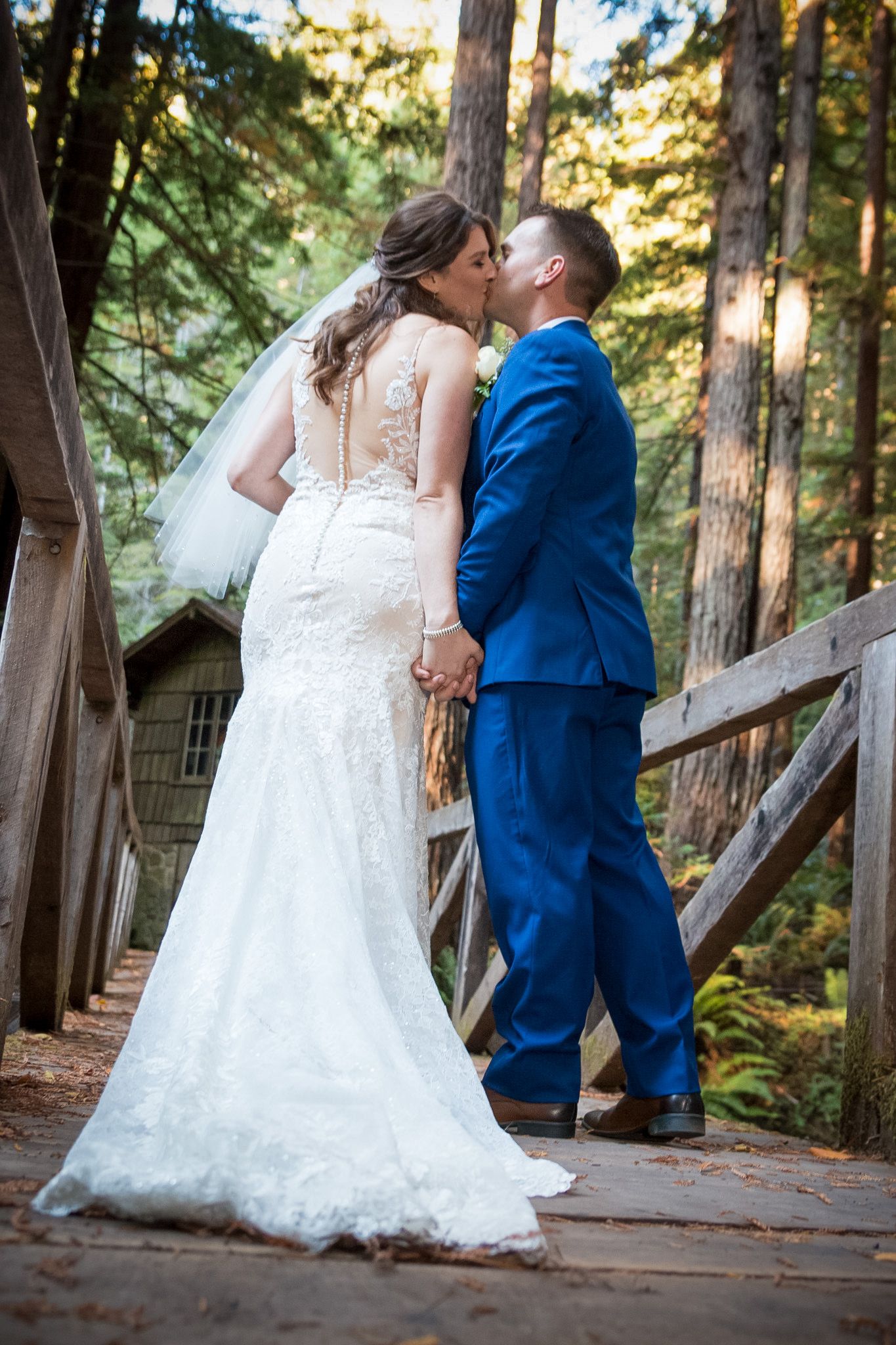 Intimate wedding moment between newlyweds on a rustic wooden bridge in a forest setting.