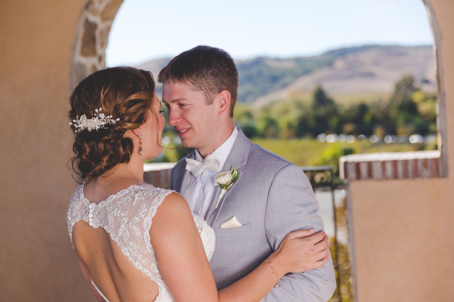 A tender moment between newlyweds under an arched doorway with scenic mountain views in the background.