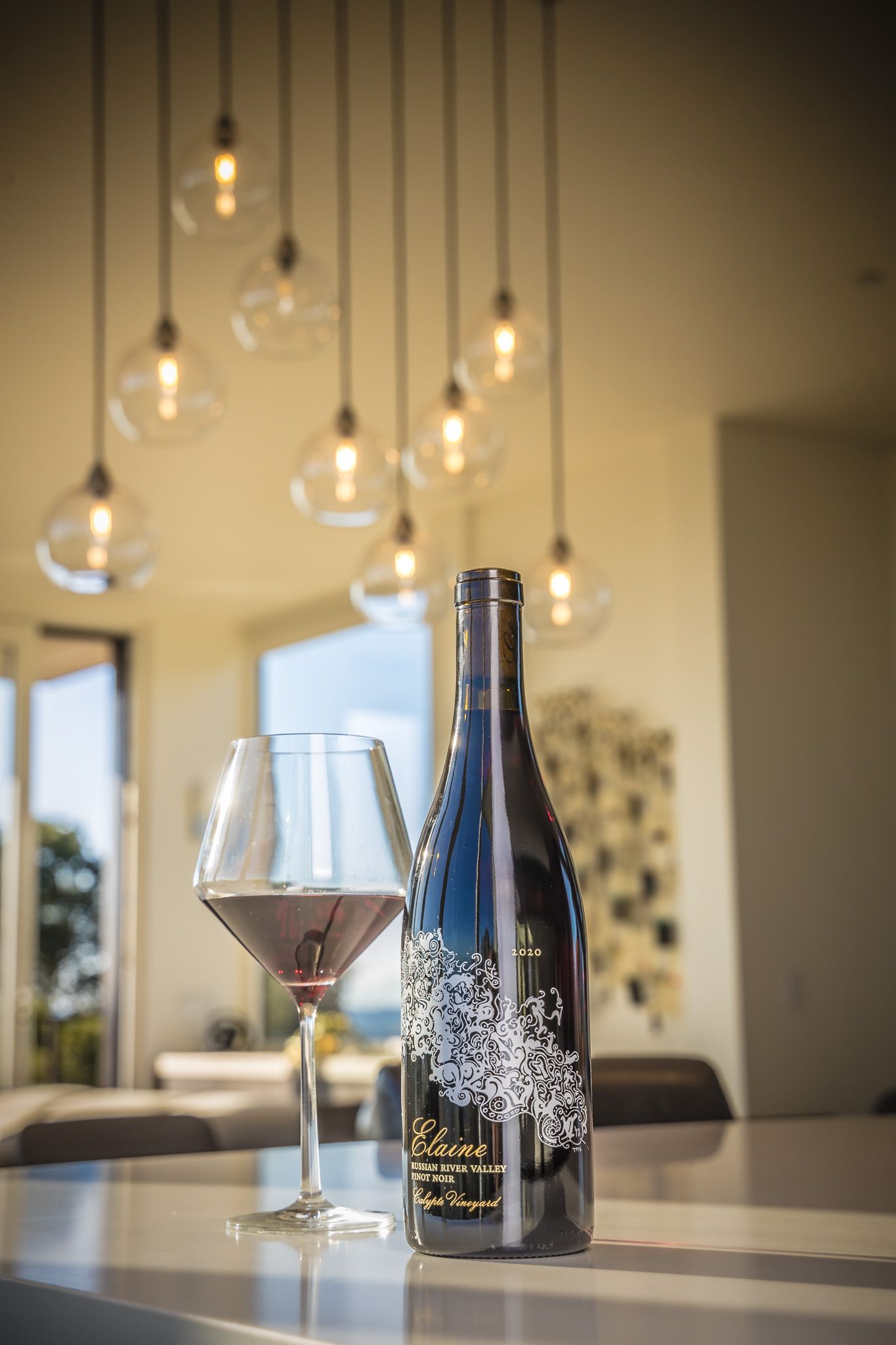 Wine bottle and glass under modern pendant lights in elegant tasting room.
