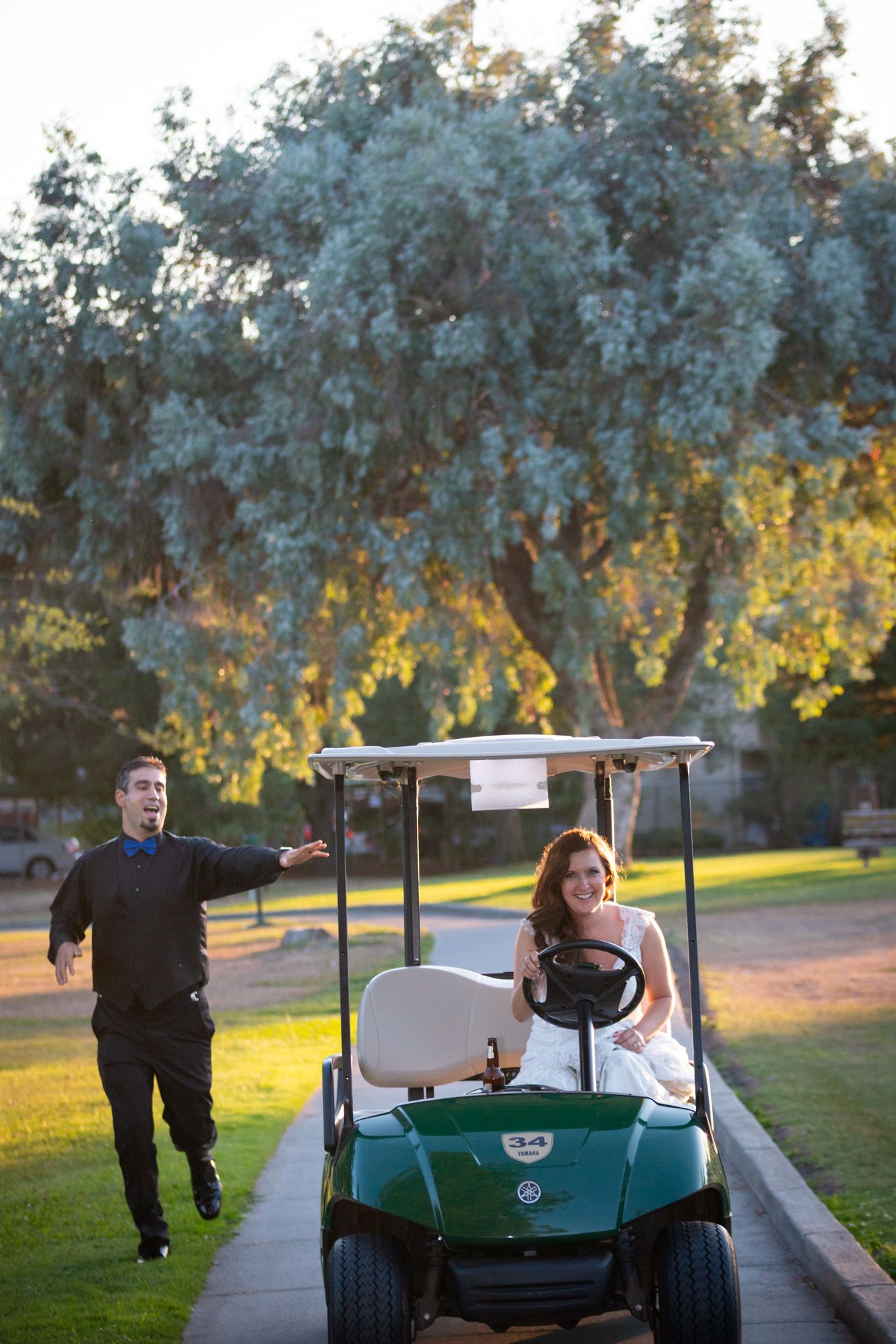 Playful wedding moment with couple on golf cart path at sunset.