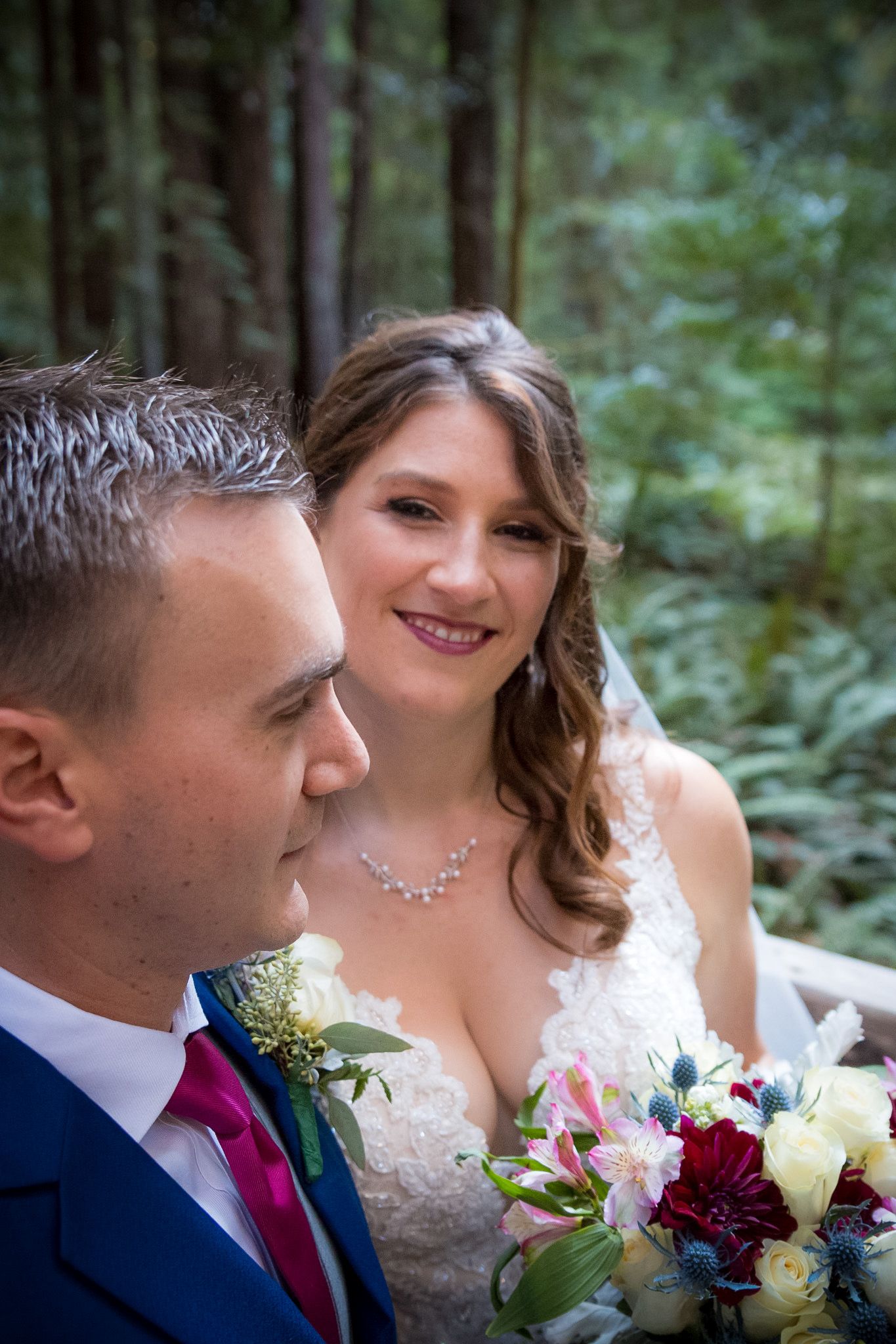 A tender moment between newlyweds with colorful wedding bouquet in a forest setting.
