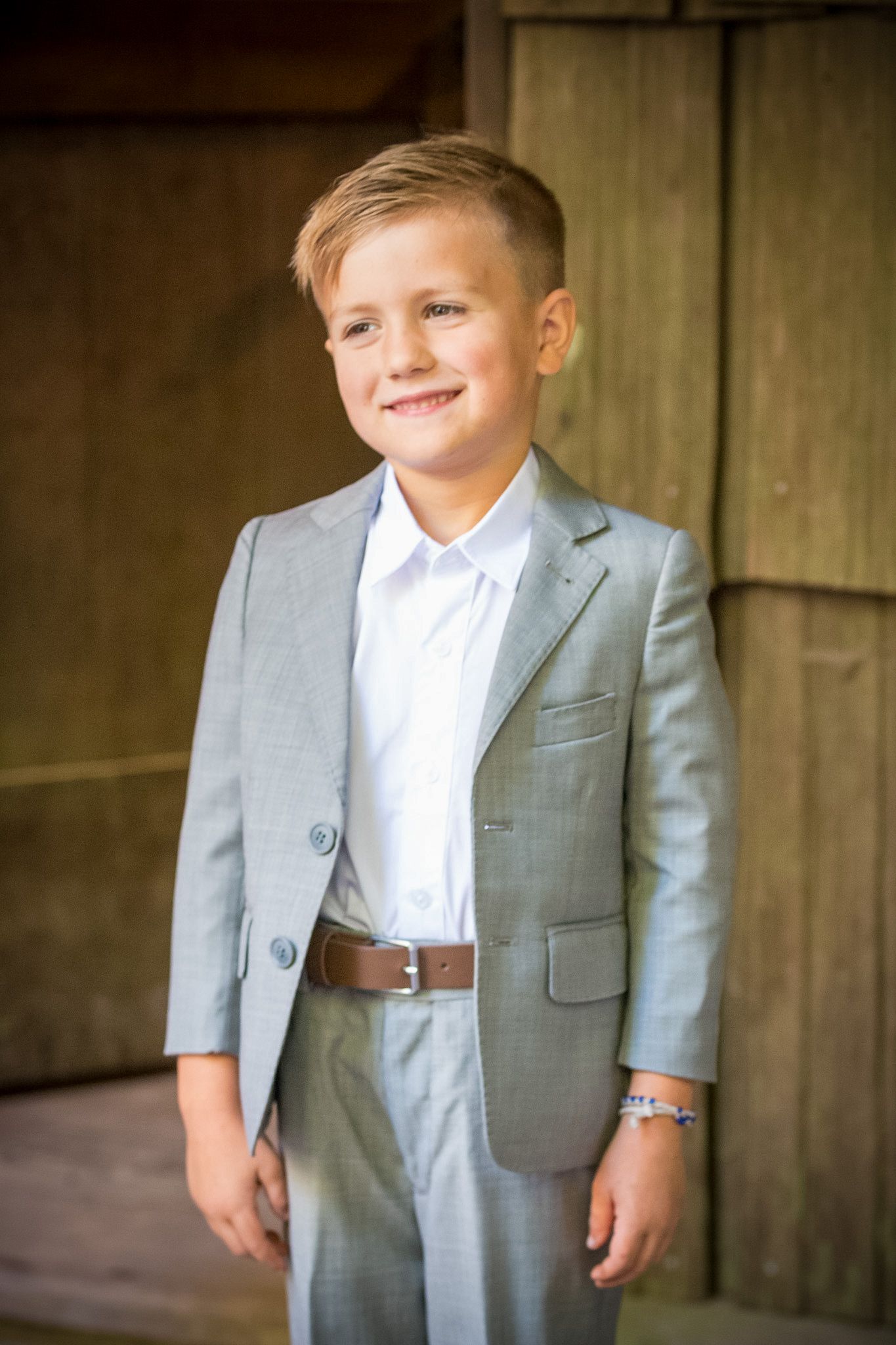 Young ring bearer in grey suit posing with bright smile.