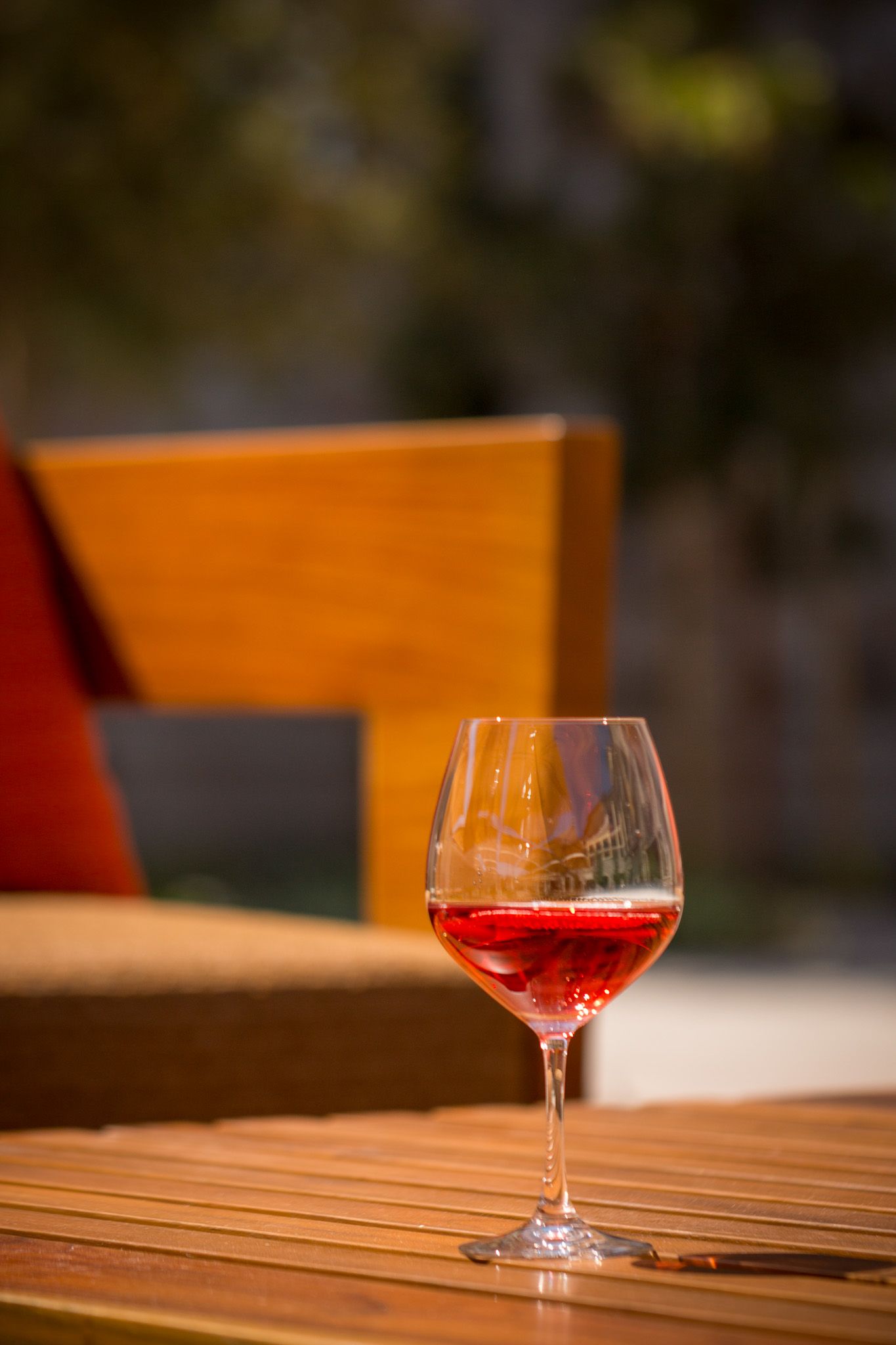 Glass of red wine on outdoor wooden table with warm lighting and orange background.