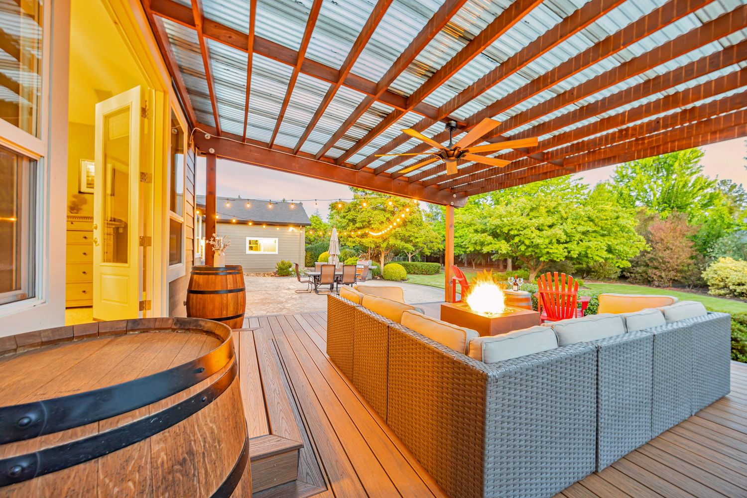 Modern outdoor deck with wooden pergola, hot tub, and comfortable patio furniture illuminated at dusk.
