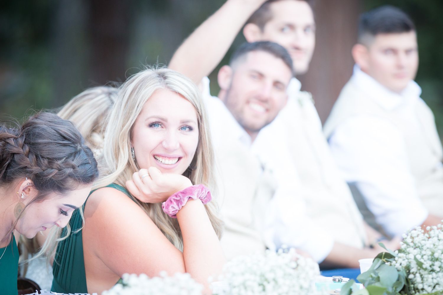 A joyful wedding reception moment with guests seated at an outdoor table smiling and laughing.