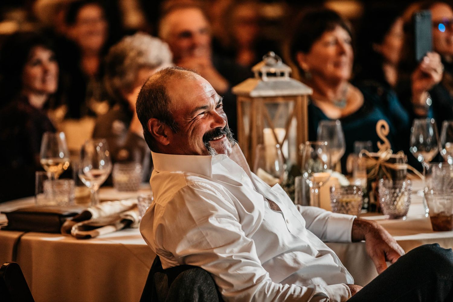 A guest laughing during the wedding reception with table settings and lantern decor visible.
