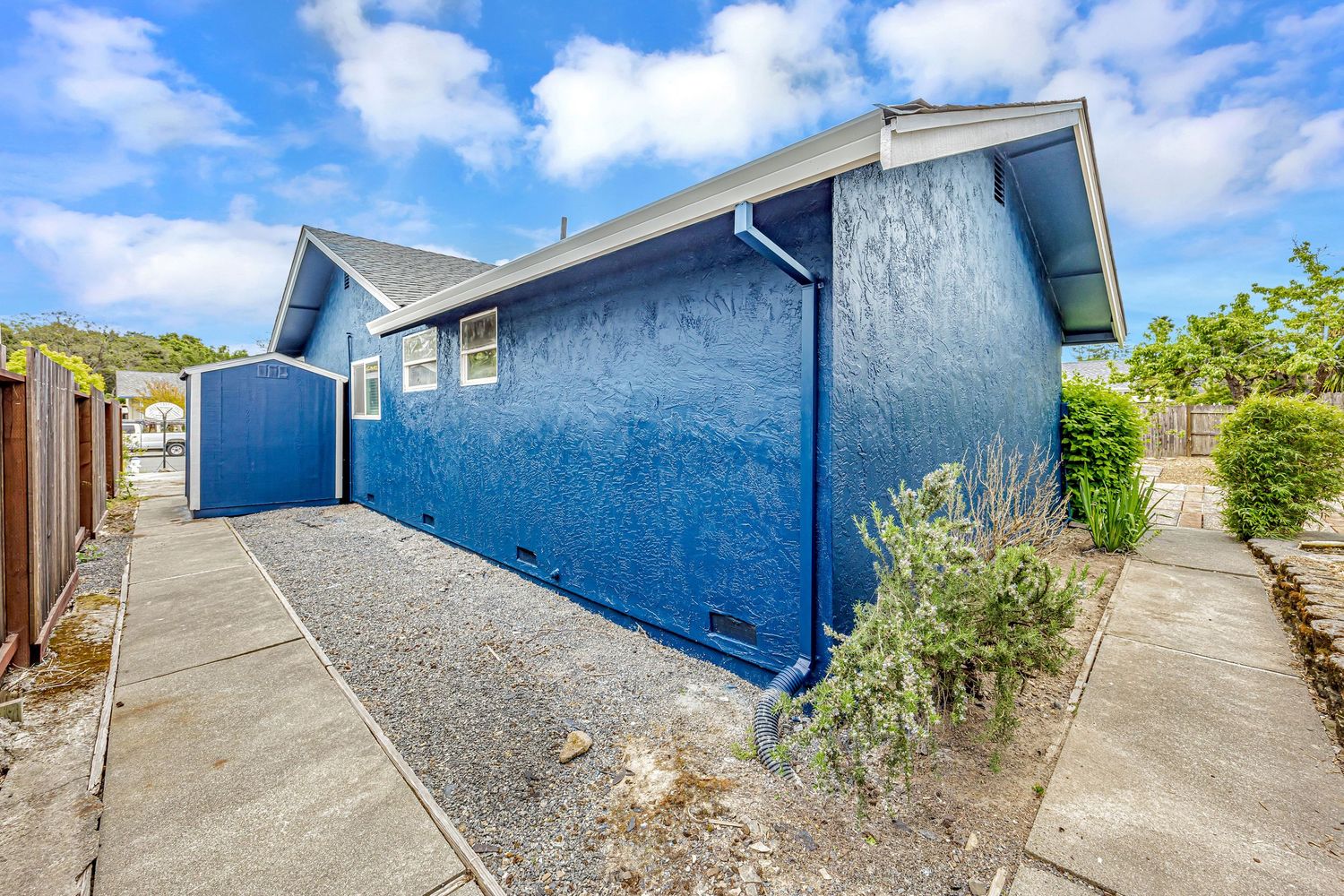 Side angle of bright blue house exterior with concrete path and minimal landscaping.