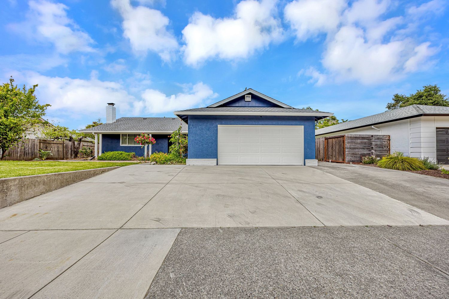 Wide concrete driveway leading to blue garage with ranch house visible in background.