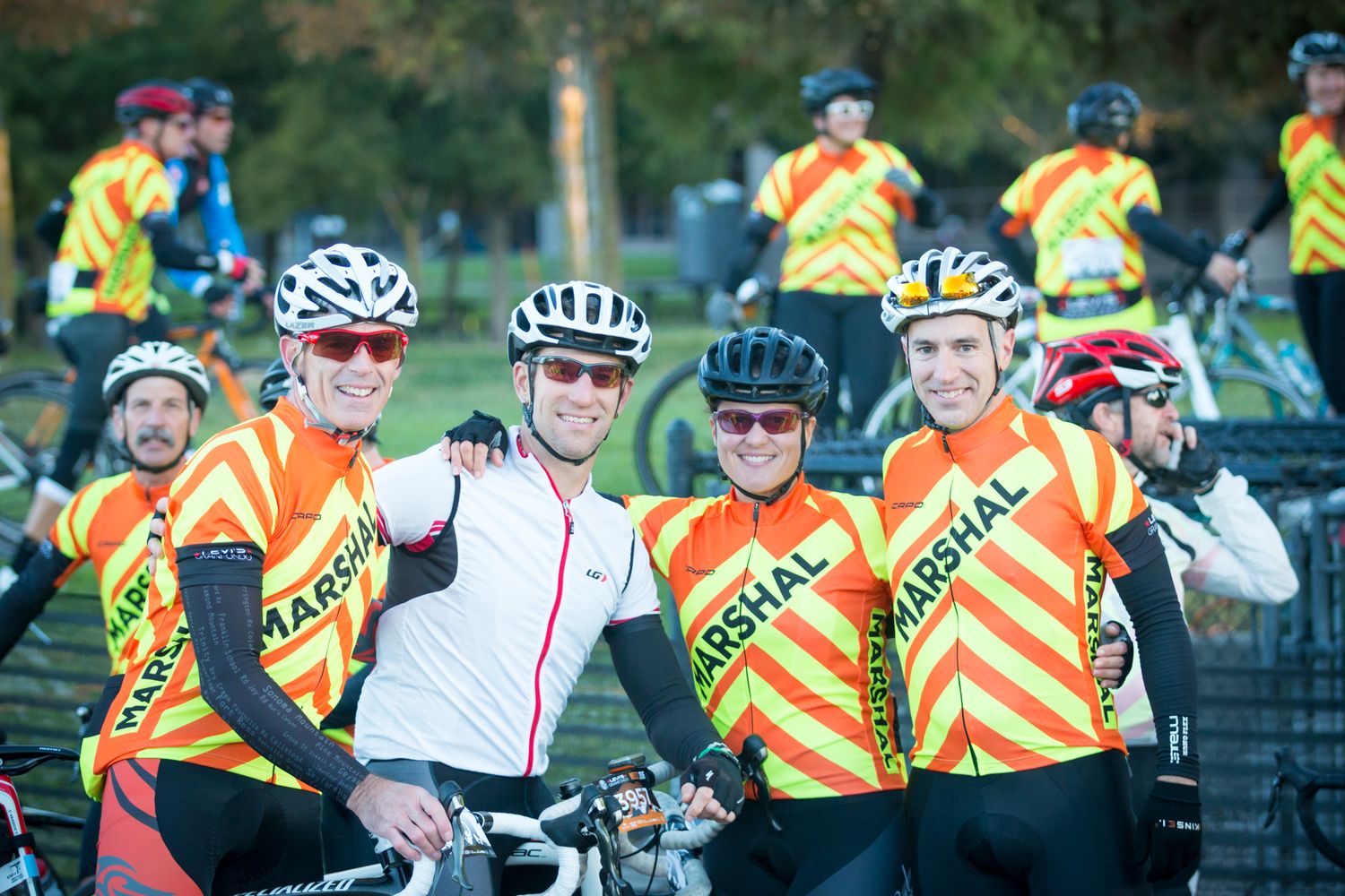 A group of cyclists in bright safety vests posing together at an outdoor cycling event.