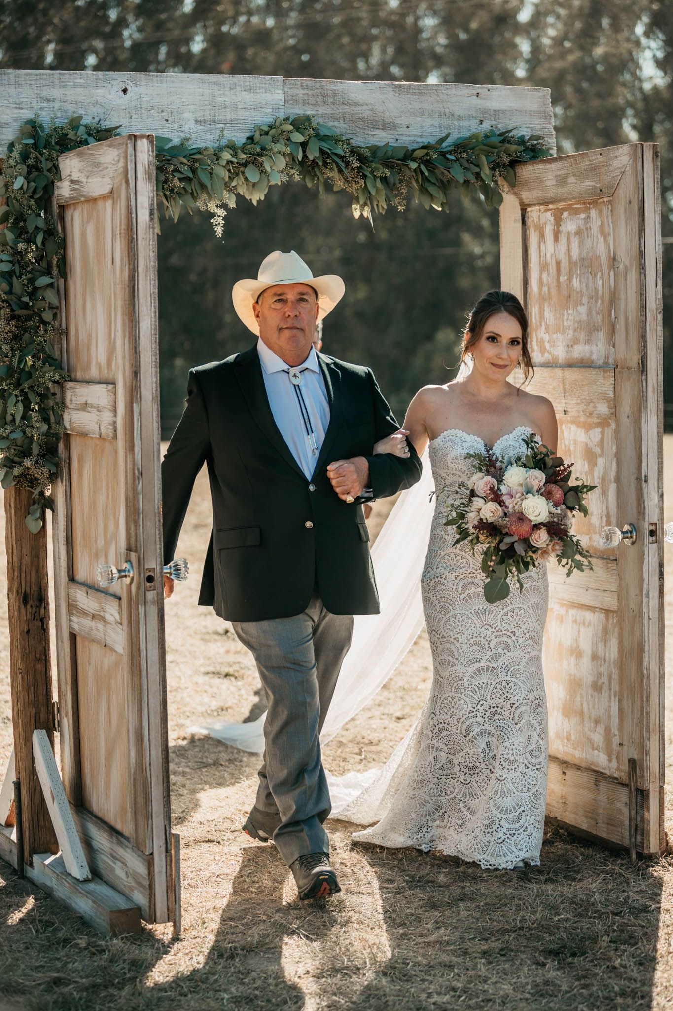 Rustic outdoor wedding ceremony entrance with vintage doors decorated in greenery.