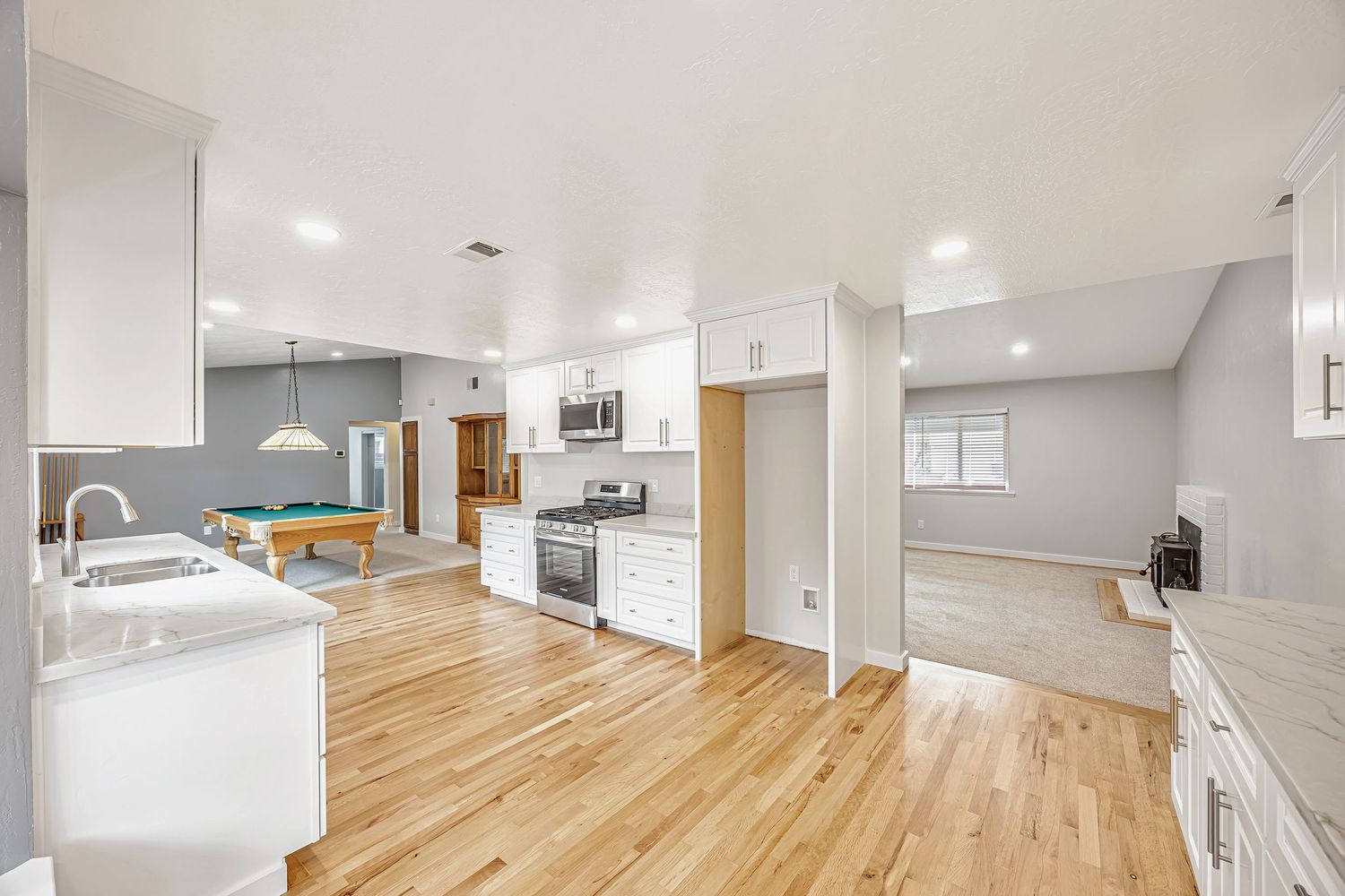 Open concept kitchen and living area with white cabinets and natural wood floors.