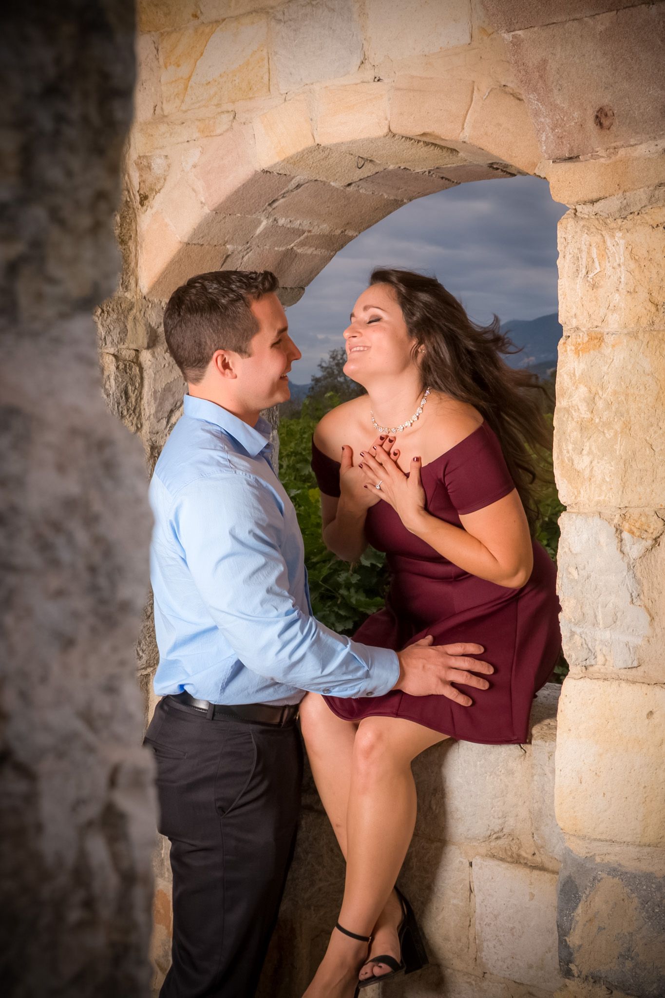 Intimate moment between couple in stone archway with mountains visible in background.
