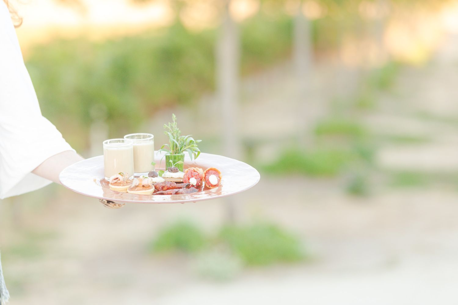Elegant plate of appetizers and drinks being served outdoors in soft focus.