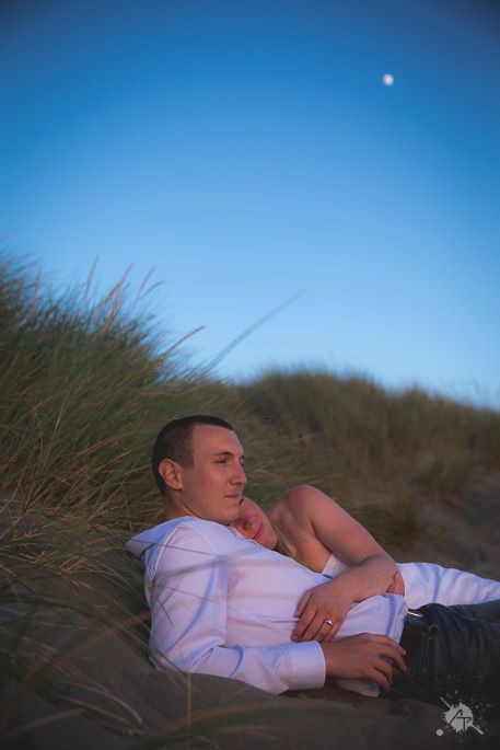 Person relaxing in white shirt against sand dunes with moon in blue sky.