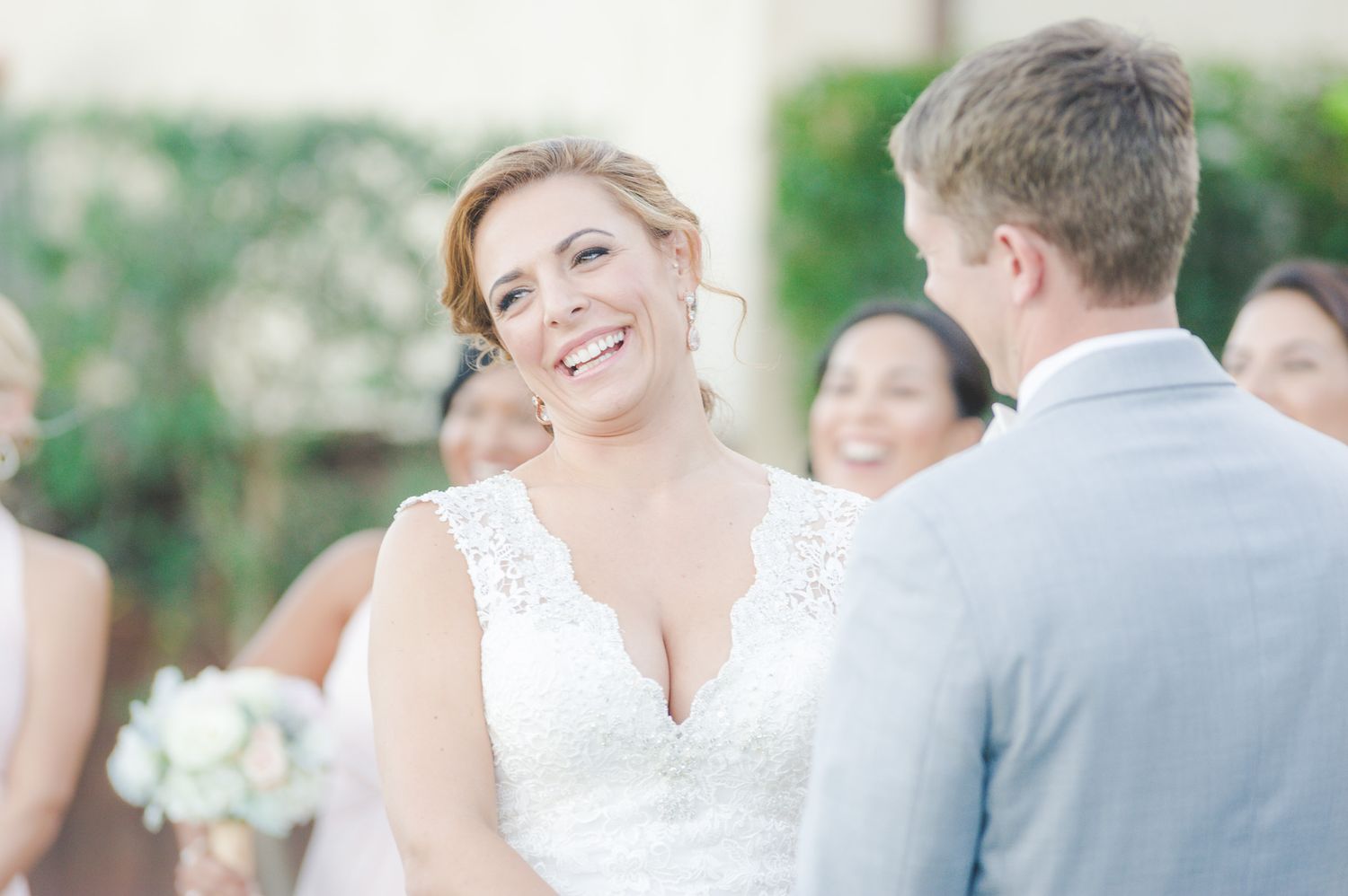 A happy wedding moment between the bride in white lace and groom in gray during an outdoor ceremony.