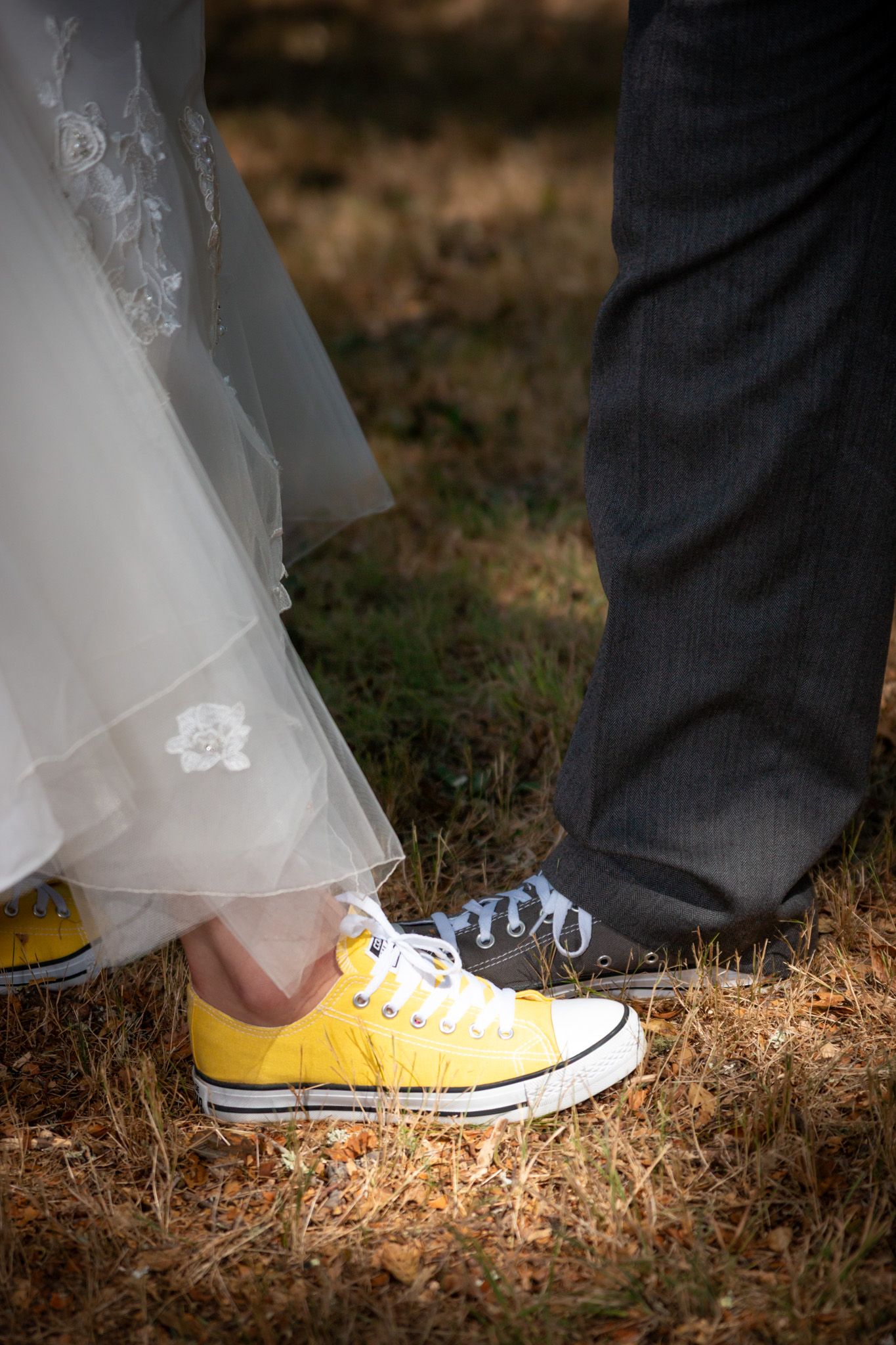 A couple wearing contrasting footwear - a white wedding dress with yellow Converse sneakers and dark formal shoes with polka dots.