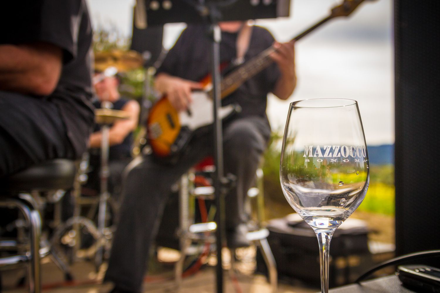 Wine glass in foreground with blurred musicians performing on stage.