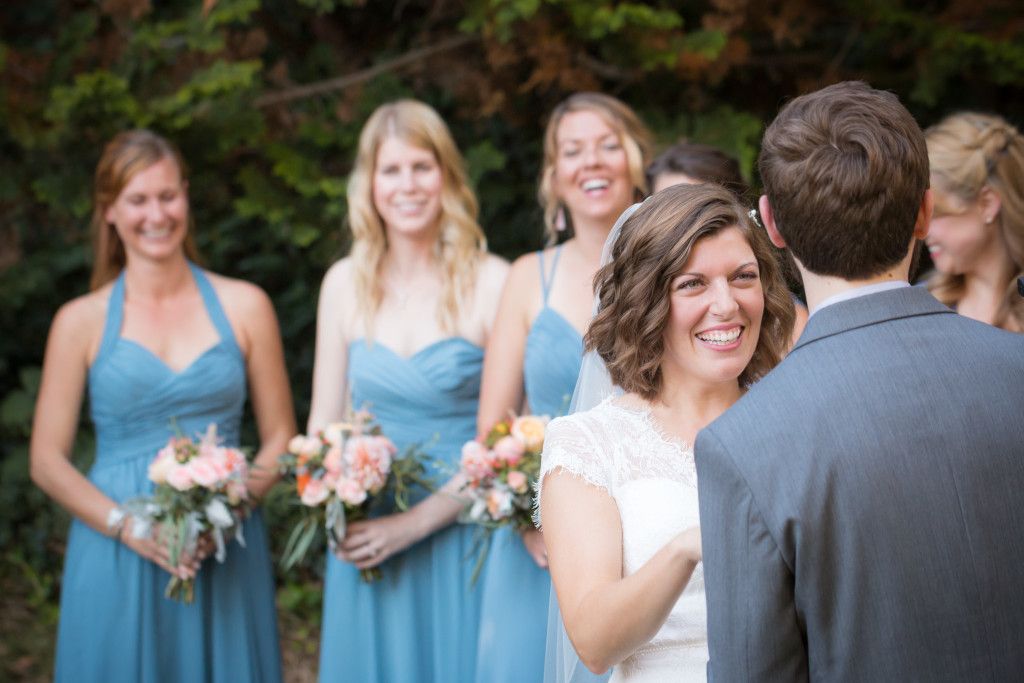 Intimate forest wedding ceremony moment with bridesmaids in blue dresses watching from background.