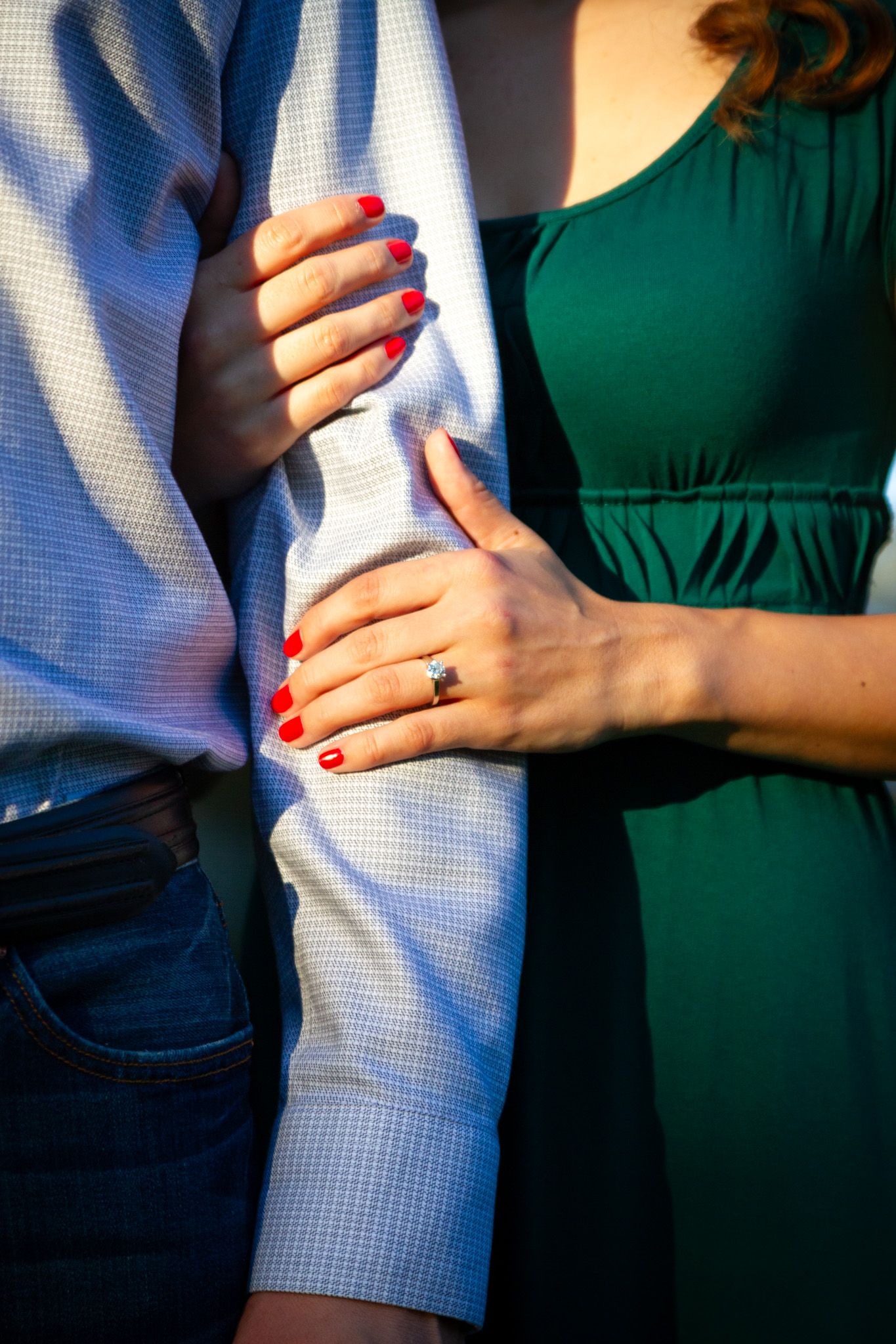 Close-up of couple's hands showing engagement ring with red nail polish against formal attire.
