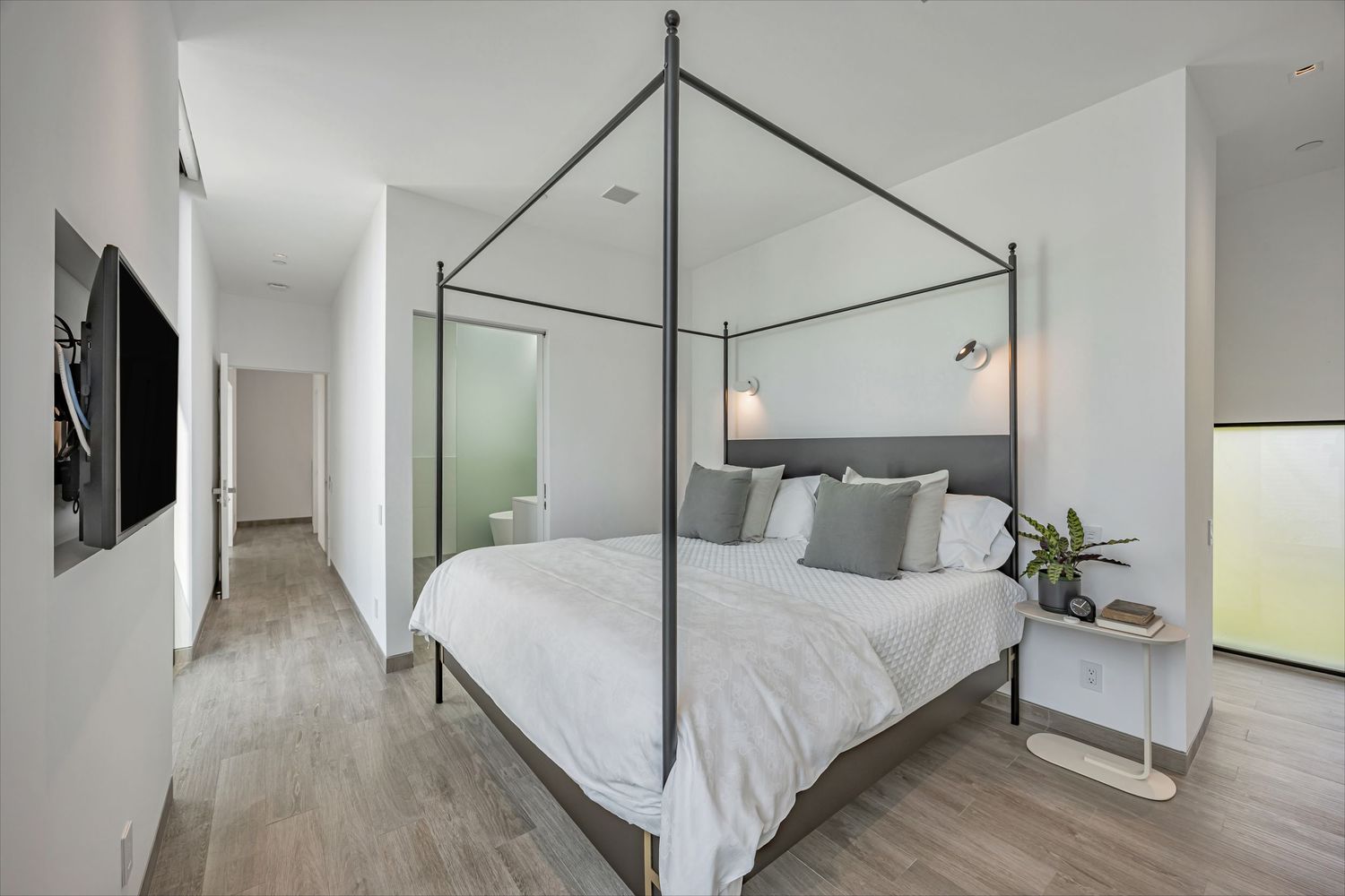Modern bedroom with a sleek canopy bed frame, white bedding, and floor-to-ceiling windows in a minimalist design.