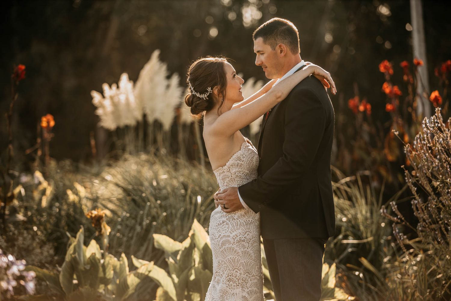 A romantic sunset embrace between newlyweds surrounded by tall grasses and wildflowers.