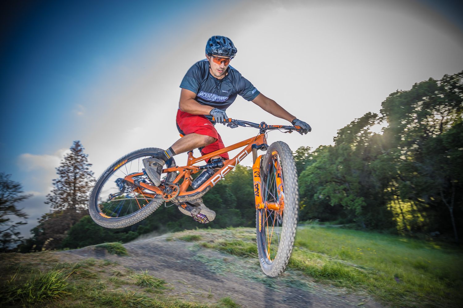 Sequence of mountain bike jumps and tricks at sunset on a dirt track.