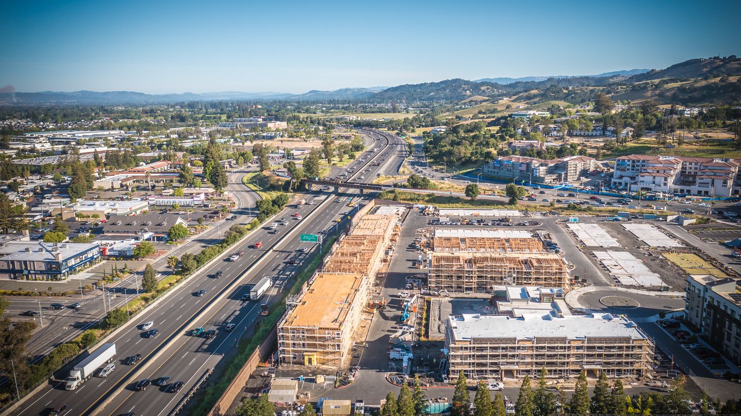 Aerial view of commercial development and roadways in suburban area with mountains.