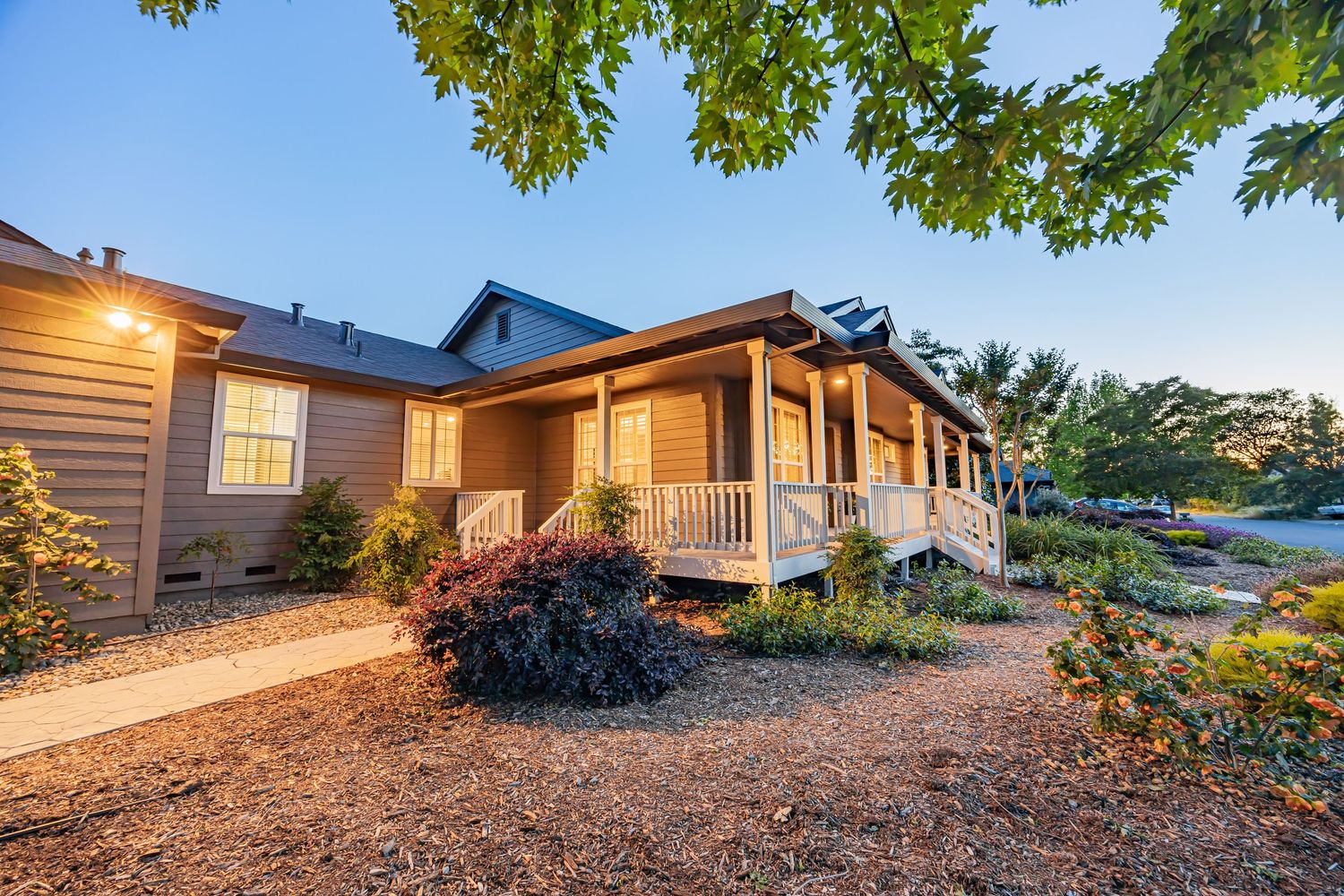 Craftsman style home with covered porch illuminated at dusk featuring natural landscaping.