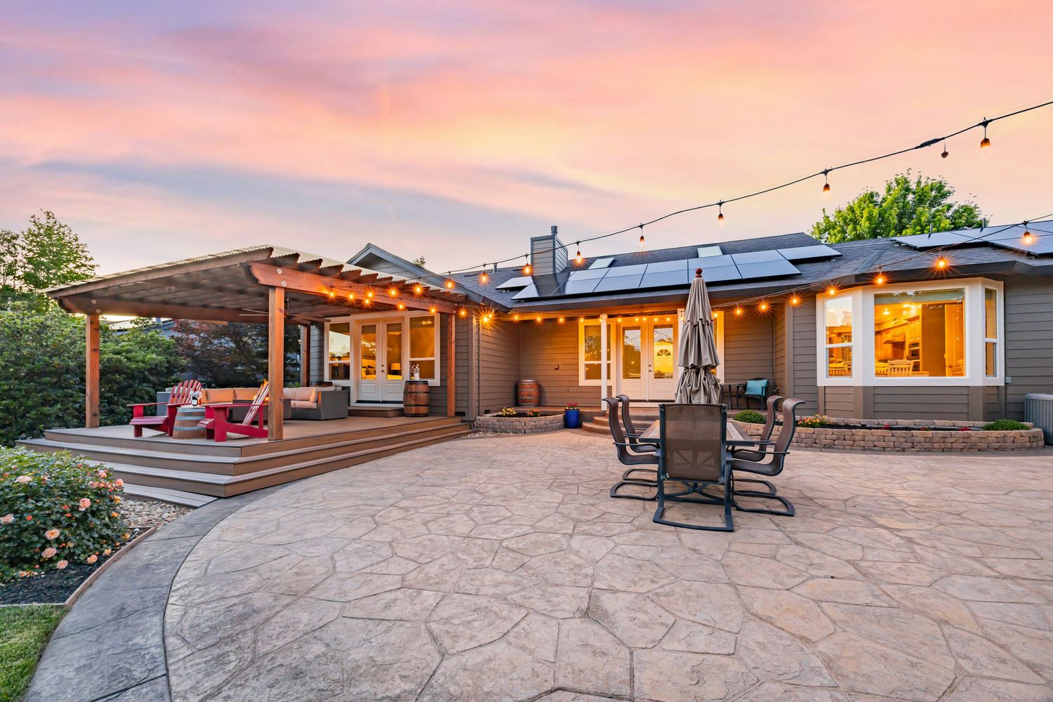 Elegant backyard patio space with string lights and outdoor furniture set against pink evening sky.