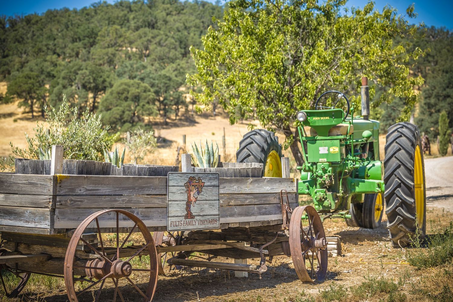 Vintage wooden wagon and green tractor displayed in rustic farm setting.
