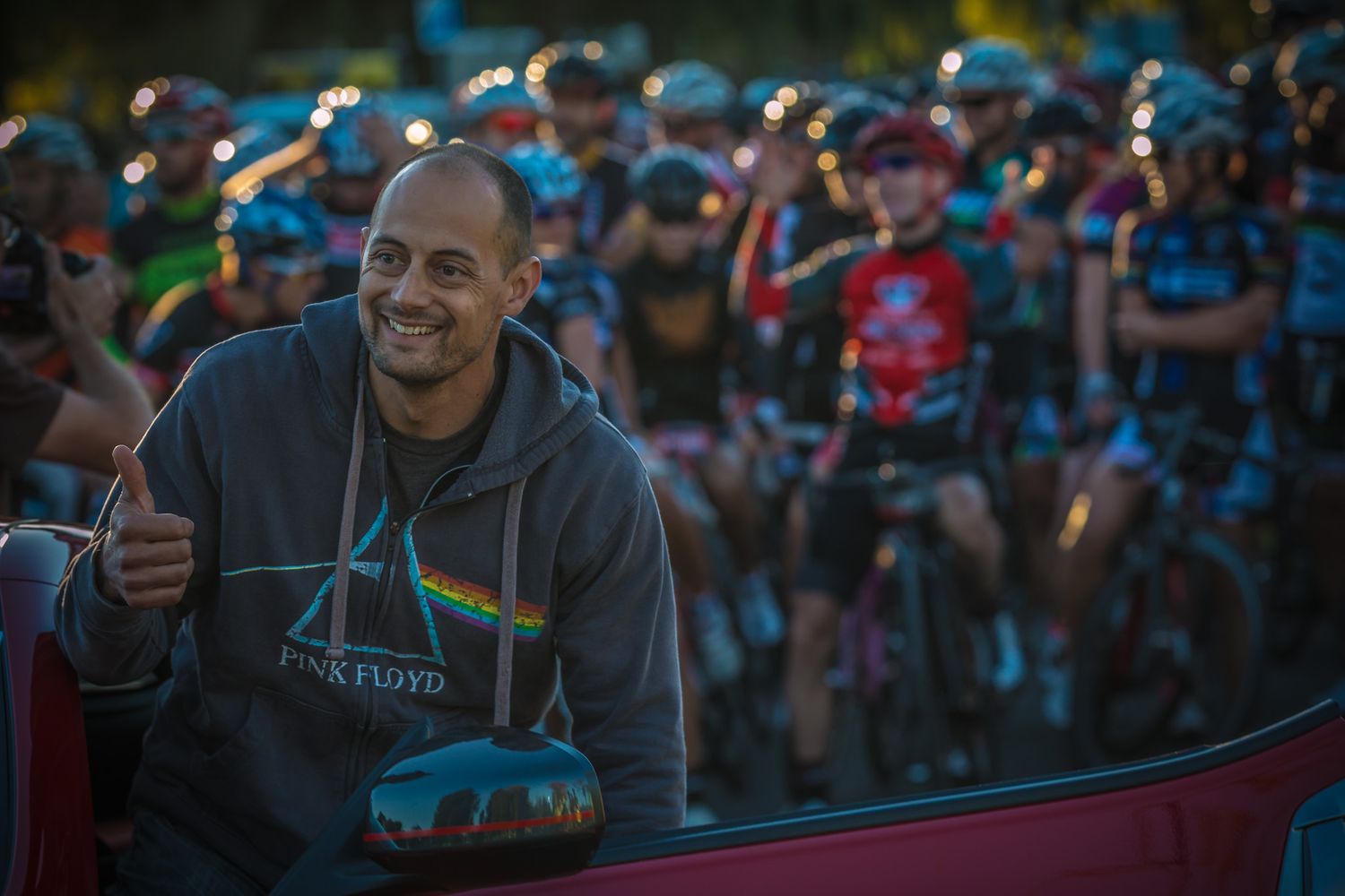 A spectator gives thumbs up while watching a cycling event from inside a vehicle.