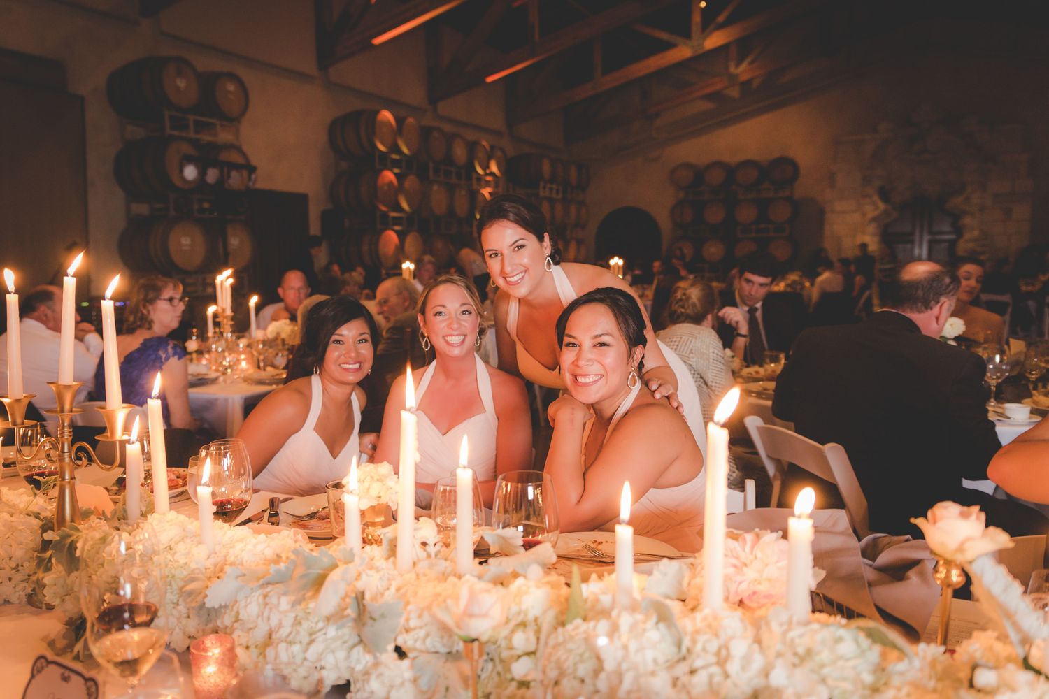 Wedding guests enjoy an elegant candlelit dinner reception at a rustic venue with glowing ambiance.
