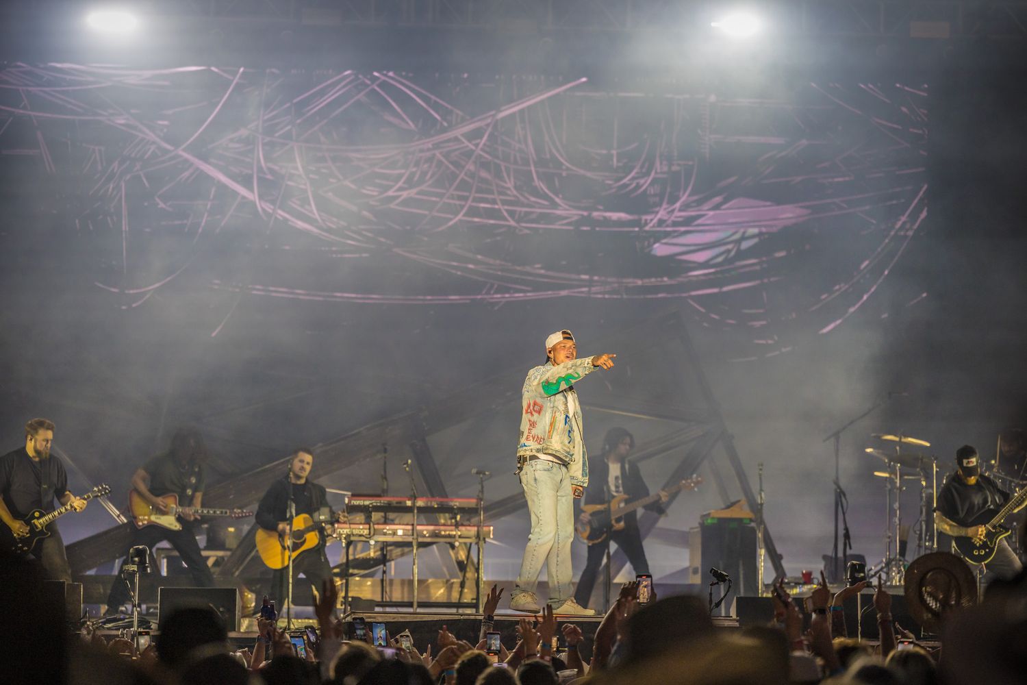 Musical performer on stage surrounded by band members with dreamy purple lighting effects and fog in the background.