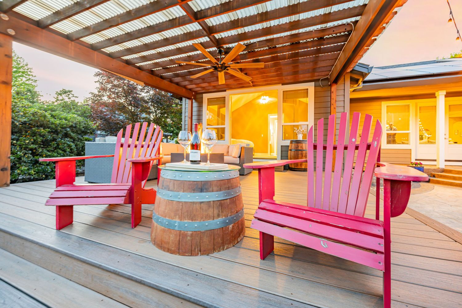 Wooden deck features pink Adirondack chairs and rustic barrel under translucent pergola roof.