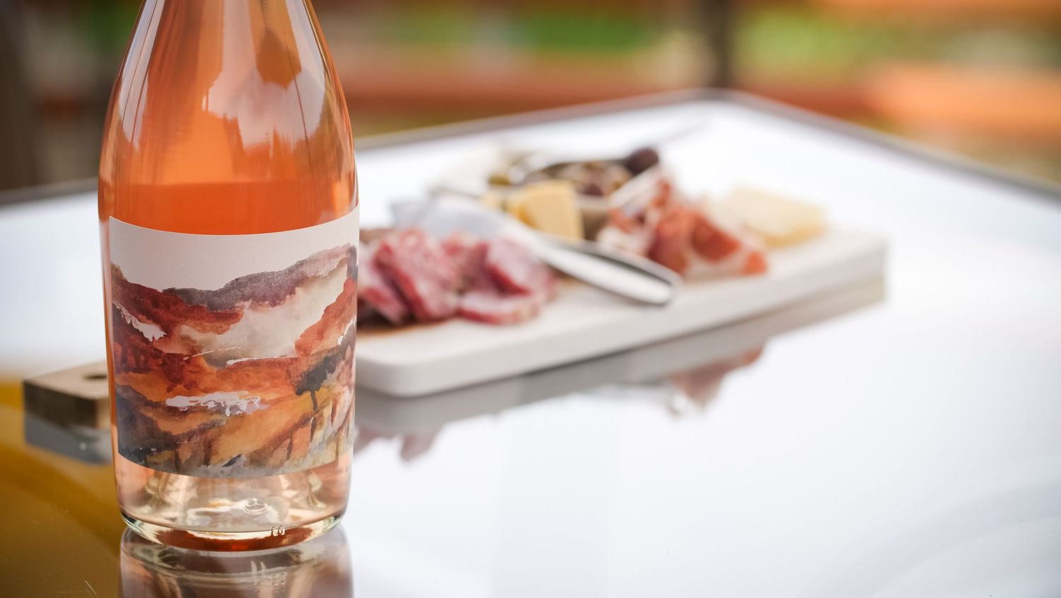 Rose wine bottle and charcuterie board on white table setting.