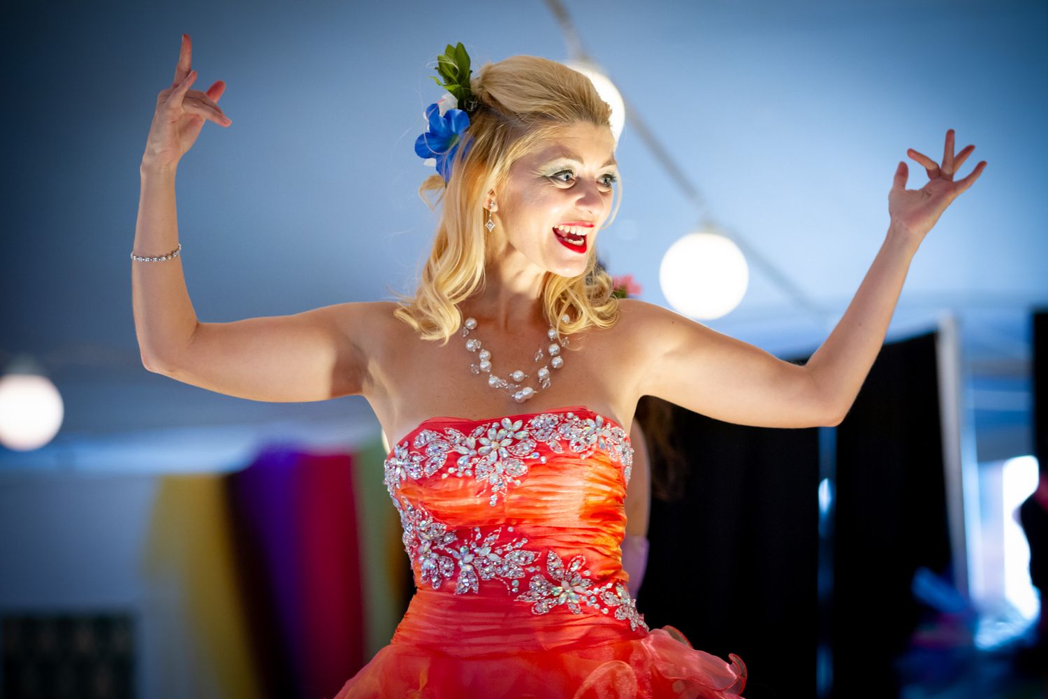 A person in an orange sequined dress dances energetically with raised arms.