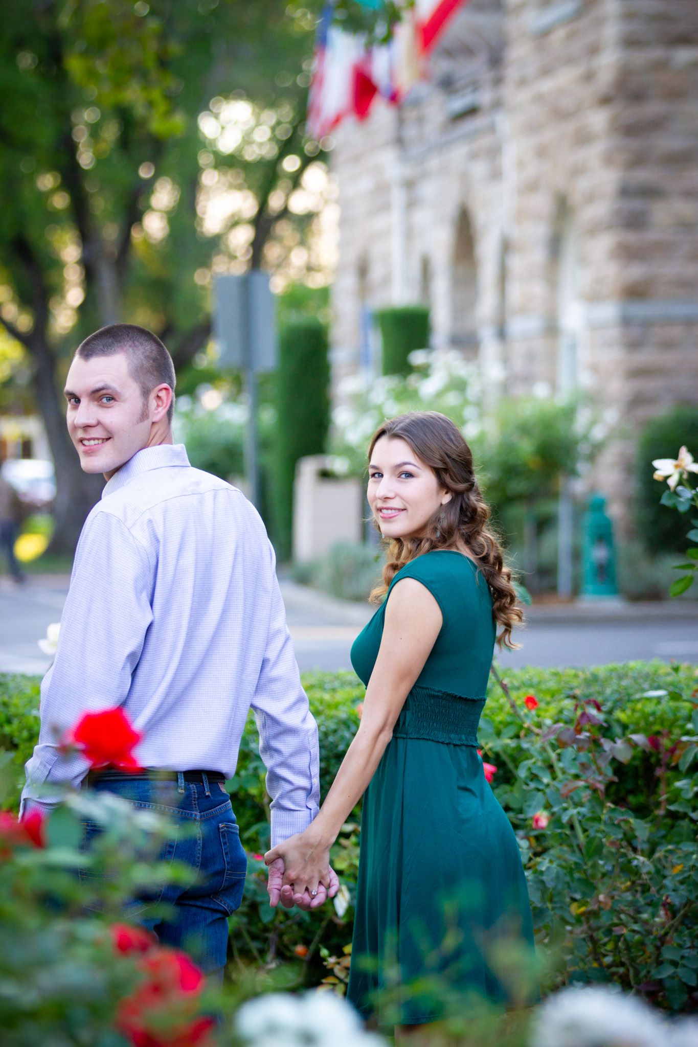 Romantic couple in formal wear holding hands while walking through garden with flowers.