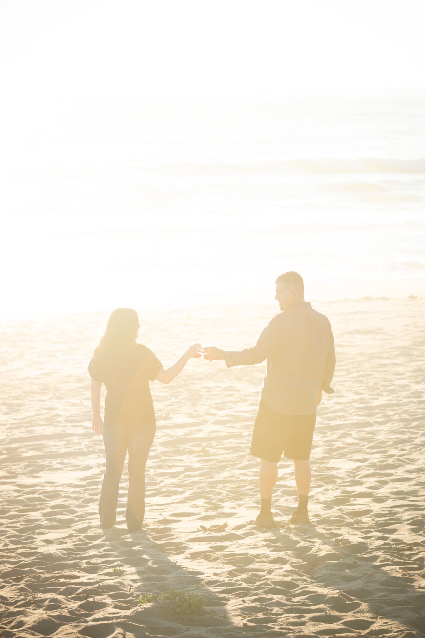 Silhouetted figures holding hands while standing on sunny beach.
