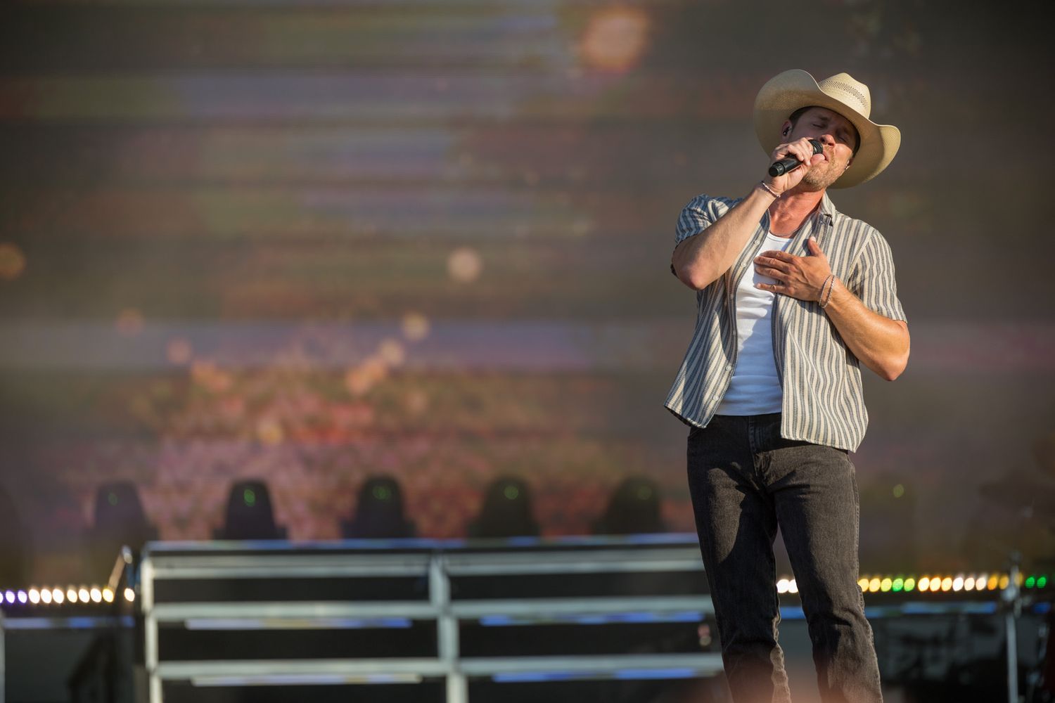 A performer sings passionately into a microphone while wearing a hat and striped shirt on an illuminated stage.